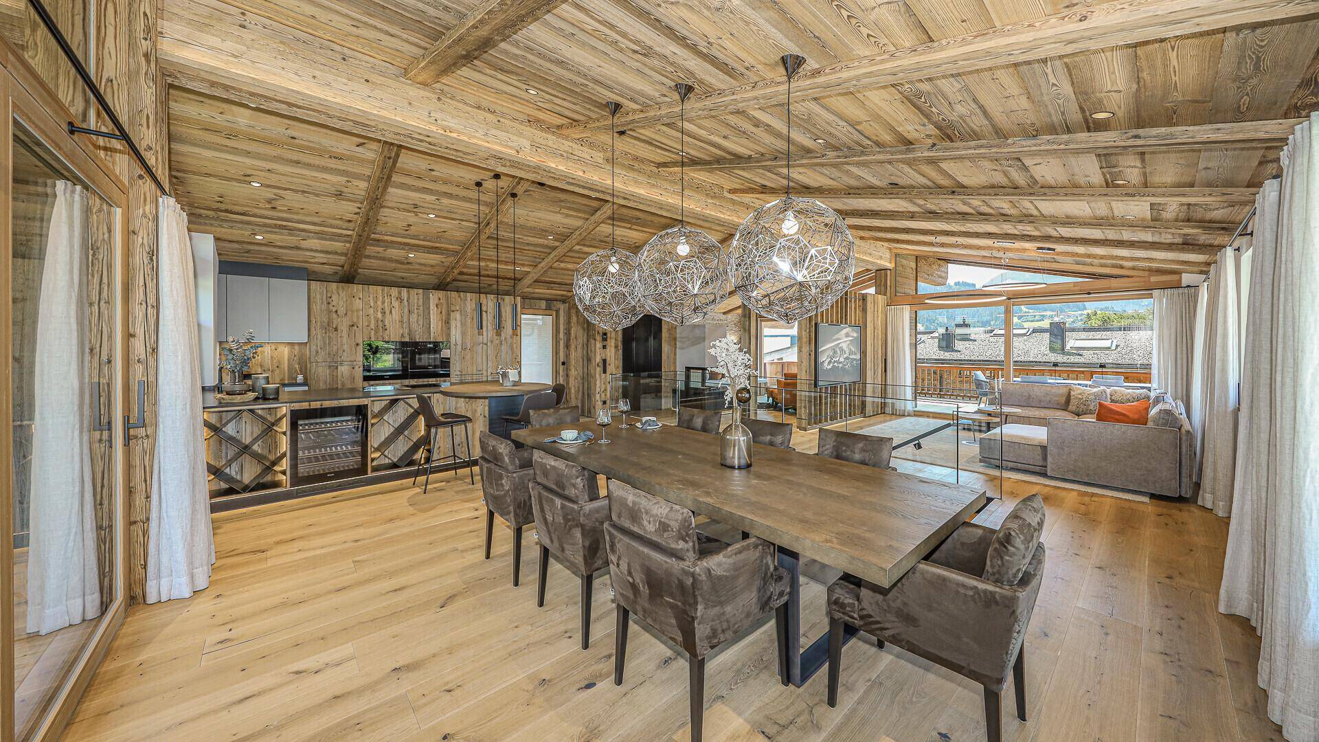 Eleganter Essbereich mit großem Holztisch, modernen Pendelleuchten und offener Küche.