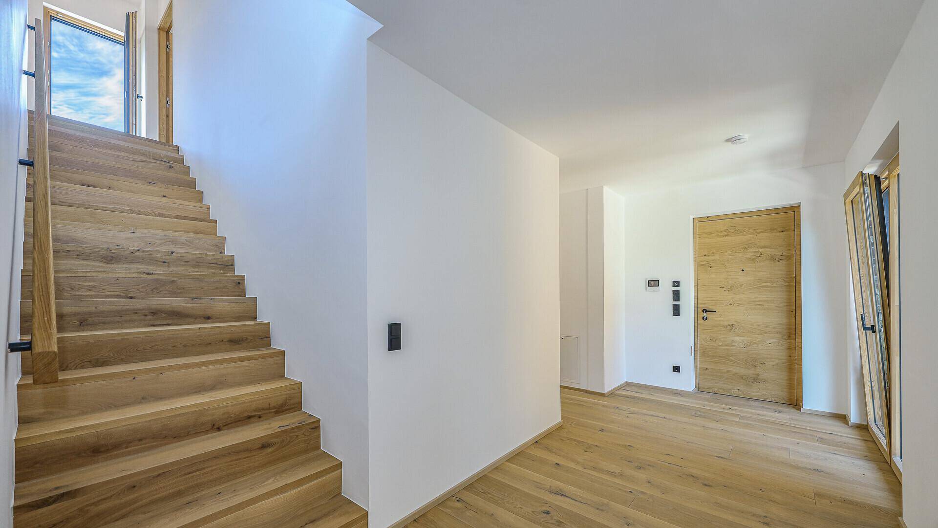 Heller Eingangsbereich mit Holztreppe und Holzboden, der zu den oberen Etagen führt.