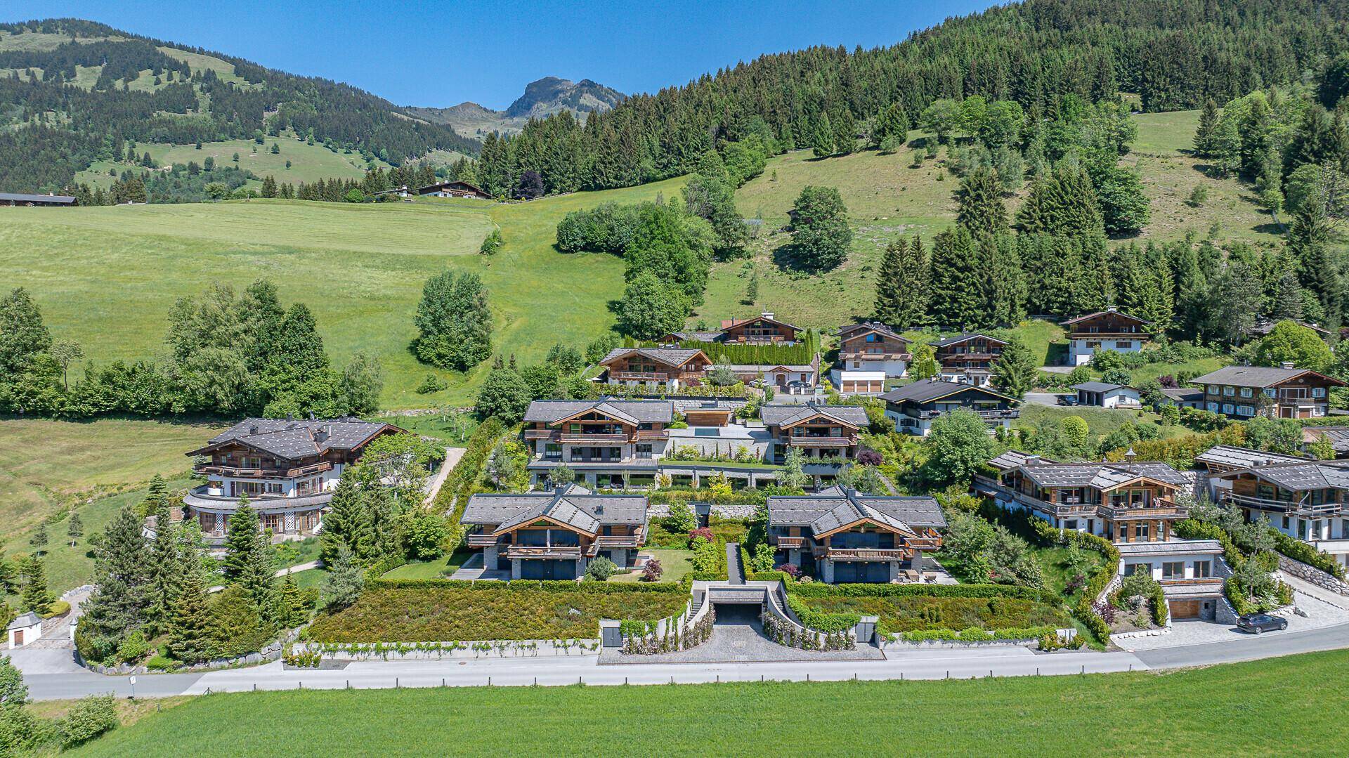 Luftaufnahme einer luxuriösen Wohnanlage im alpinen Stil, eingebettet in eine grüne Berglandschaft.