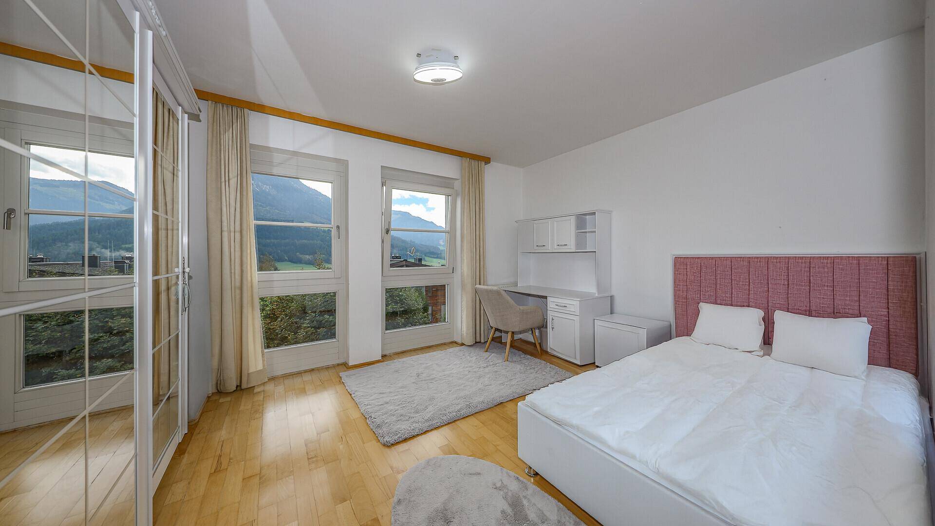 Helles Schlafzimmer mit Doppelbett, Schreibtisch und großen Fenstern mit Bergblick.