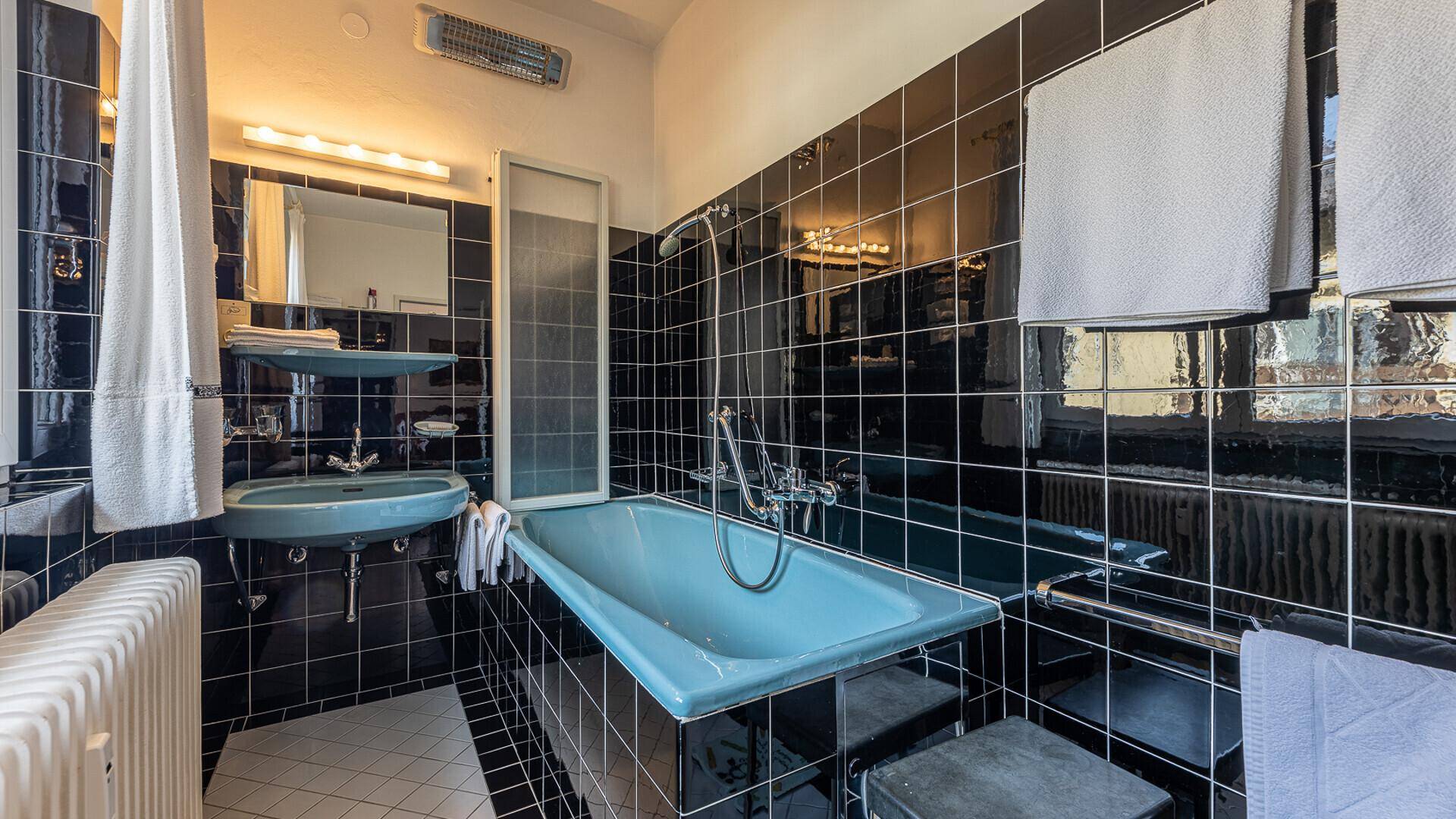 Badezimmer mit schwarzen Fliesen, einer hellblauen Badewanne und passendem Waschbecken im Retro-Stil.