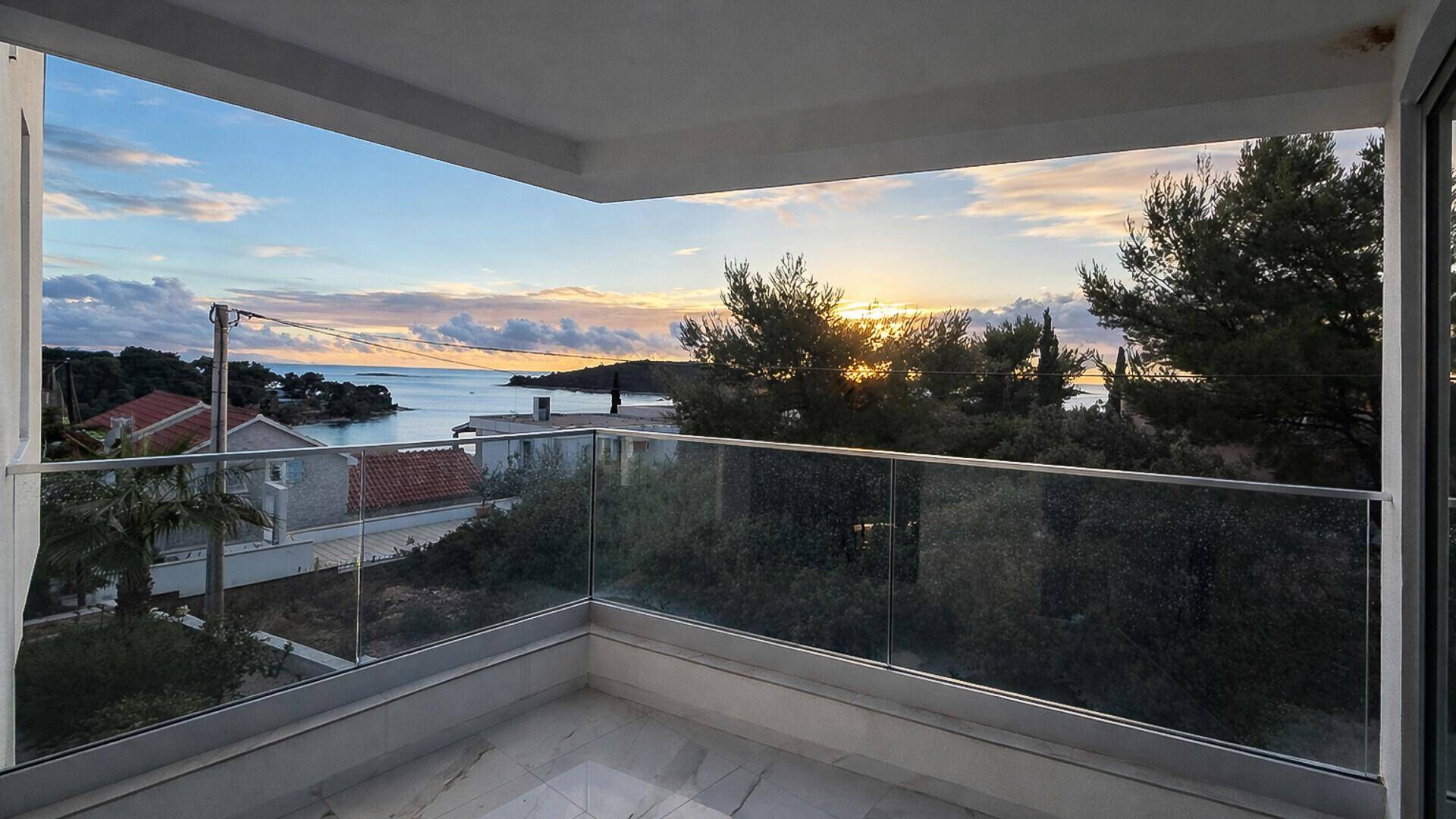 Geräumiger Balkon mit Glasgeländer und spektakulärem Meerblick bei Sonnenuntergang.