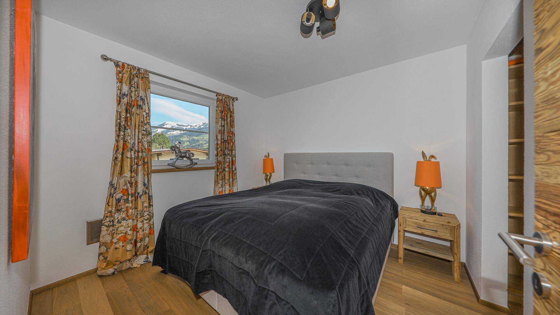 Schlafzimmer mit Doppelbett, Nachttischen und Fenster mit Blick auf die Berglandschaft.