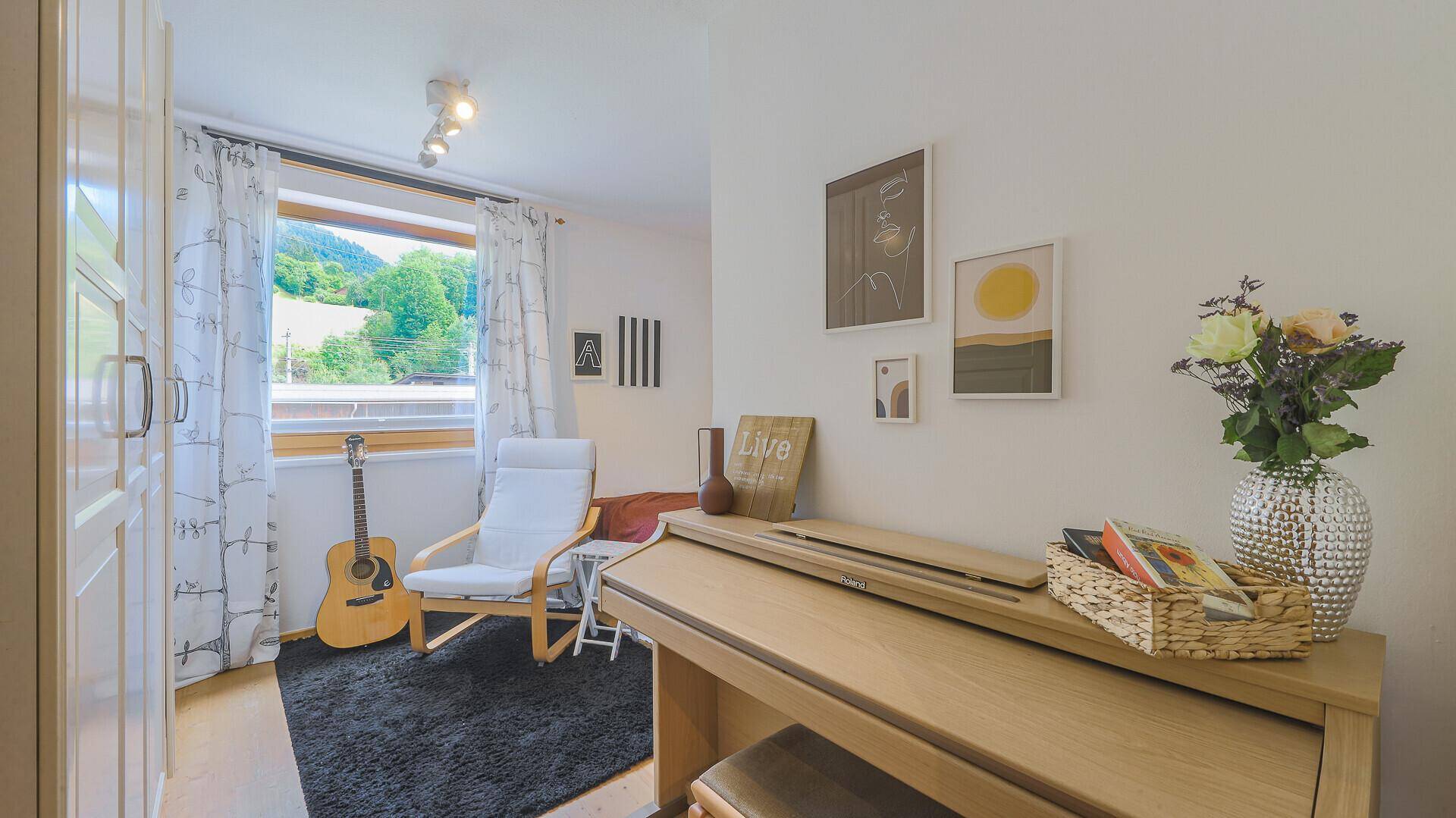 Vielseitiges Zimmer mit Klavier, Gitarre und Fenster mit Bergblick.