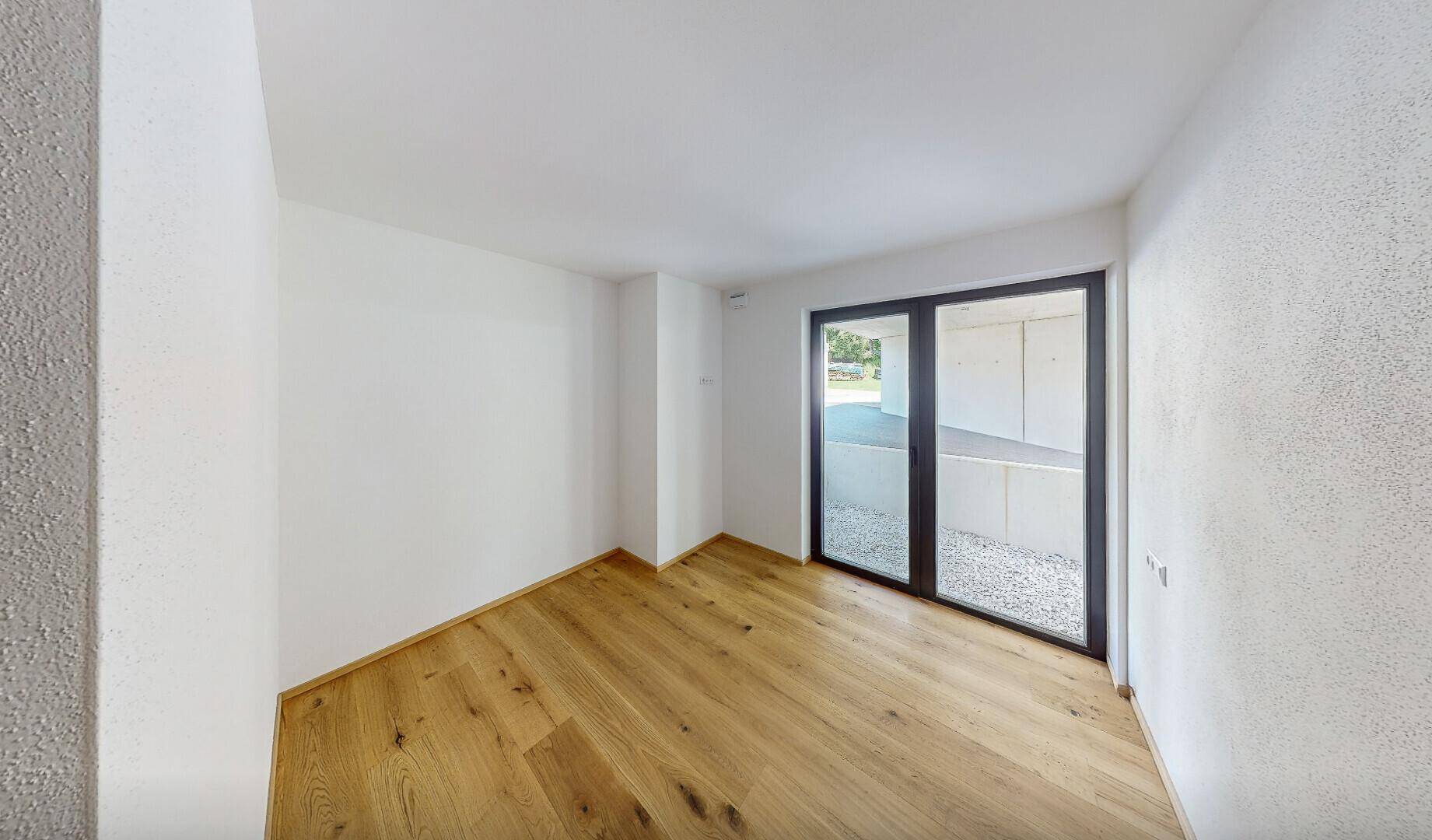 Heller, leerer Raum mit Holzboden und Zugang zu einem kleinen Außenbereich.