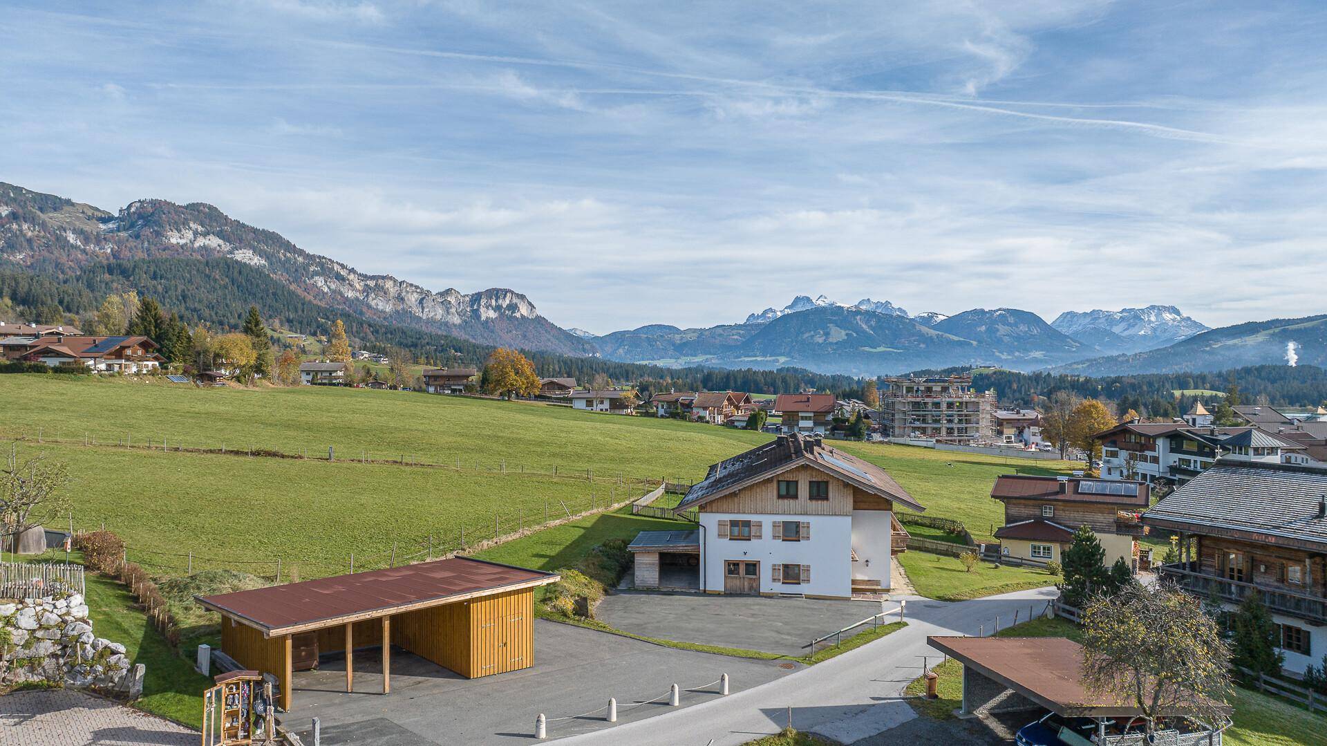 Weitläufige Landschaft mit traditionellen Häusern, grünen Wiesen und einer Bergkette am Horizont.