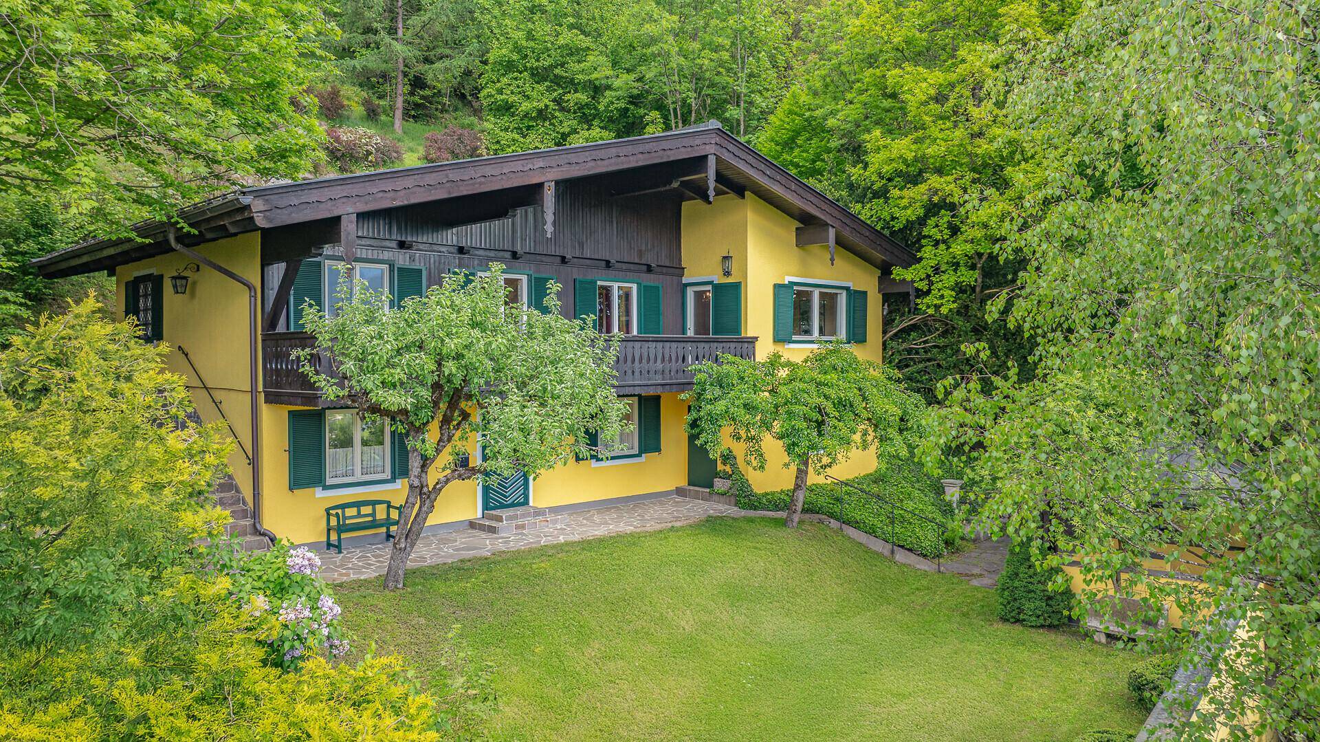 Charmantes Haus mit gelber Fassade, grünem Garten, Rasenfläche und Bergblick.