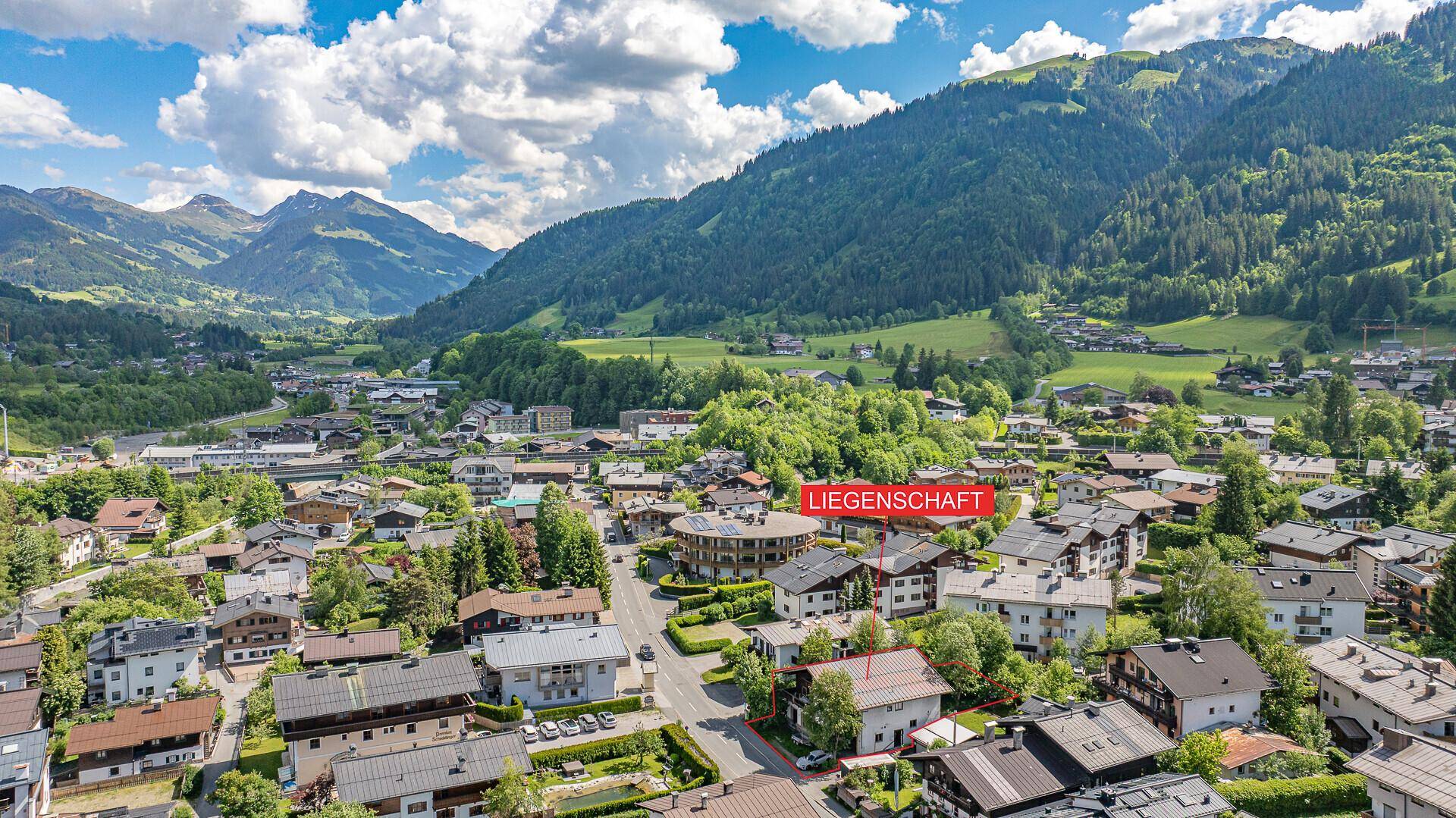 Weitläufige Luftaufnahme einer Bergstadt mit markierter Liegenschaft und grünen Hügeln.