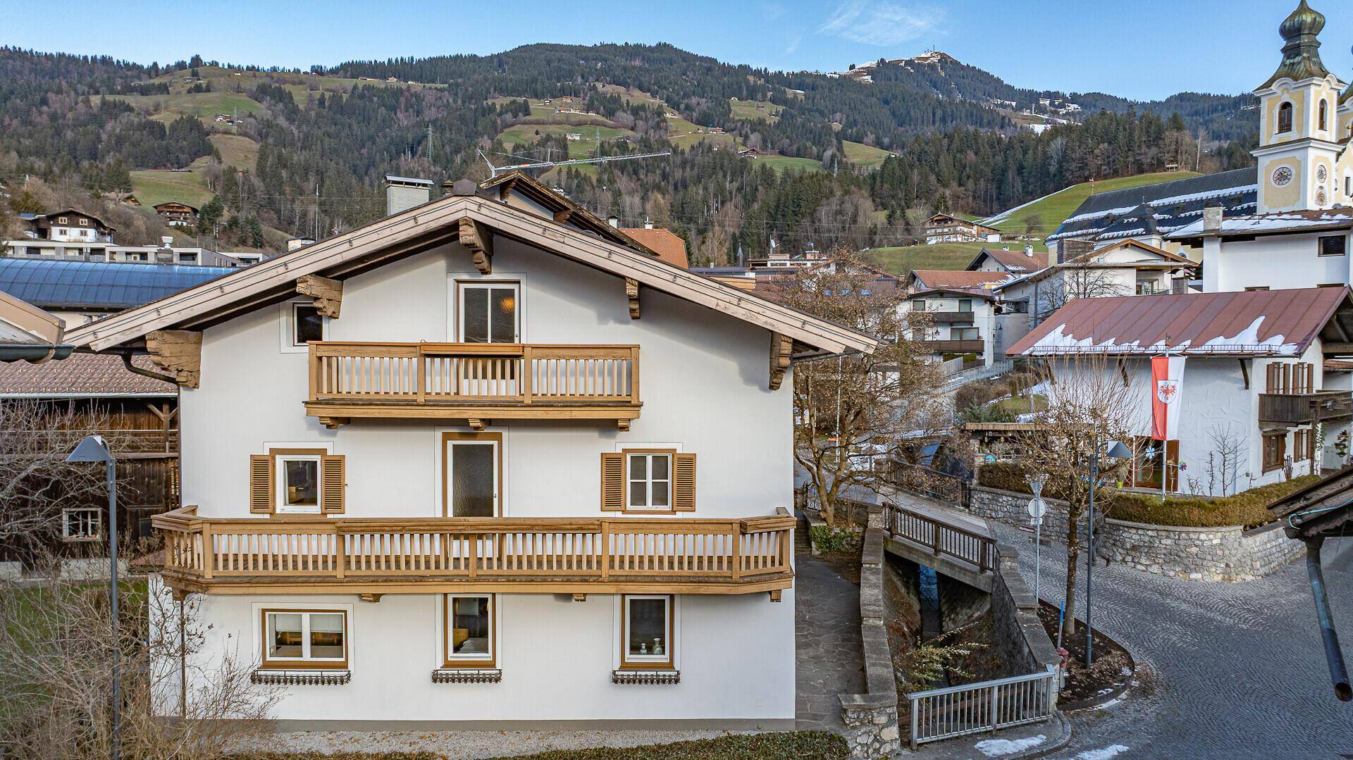 Traditionelles Haus mit mehreren Holzbalkonen und Blick auf die umliegende Berglandschaft und ein Dorf.