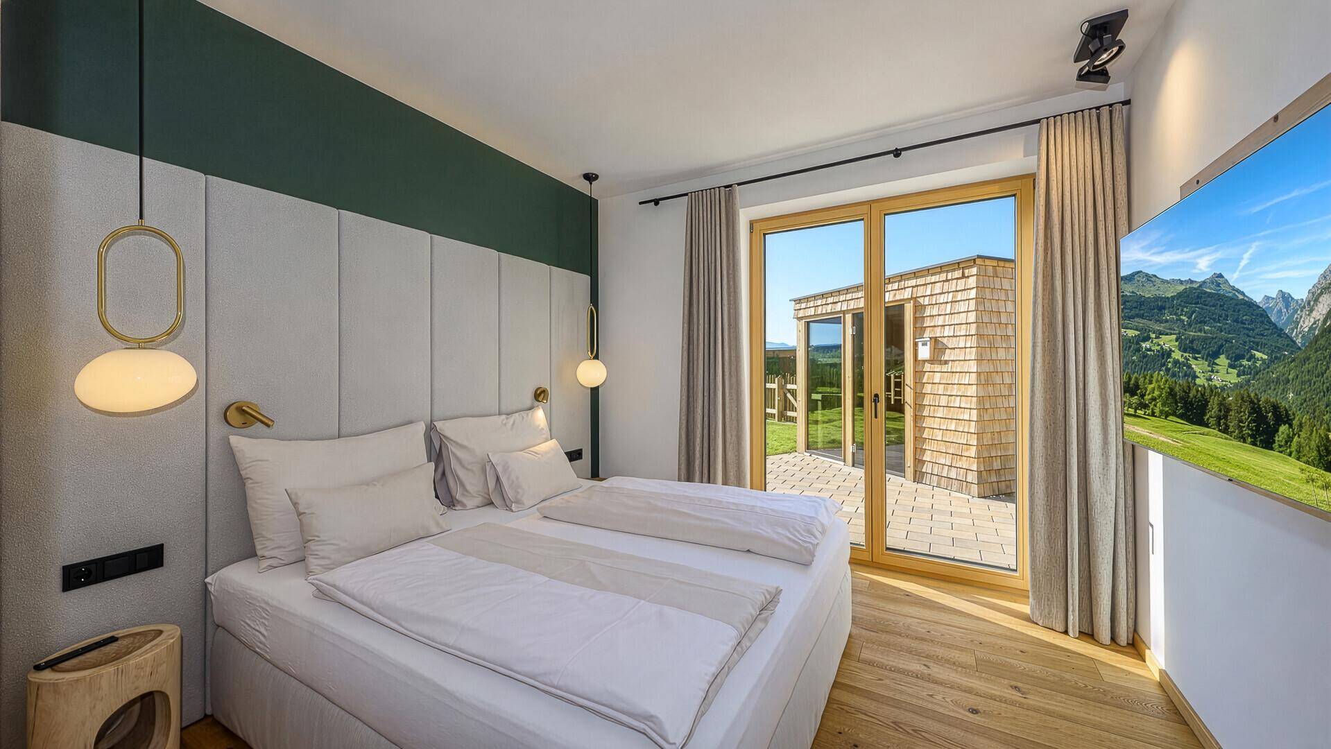 Komfortables Schlafzimmer mit Doppelbett, Holzboden und Zugang zur Terrasse mit Bergblick.