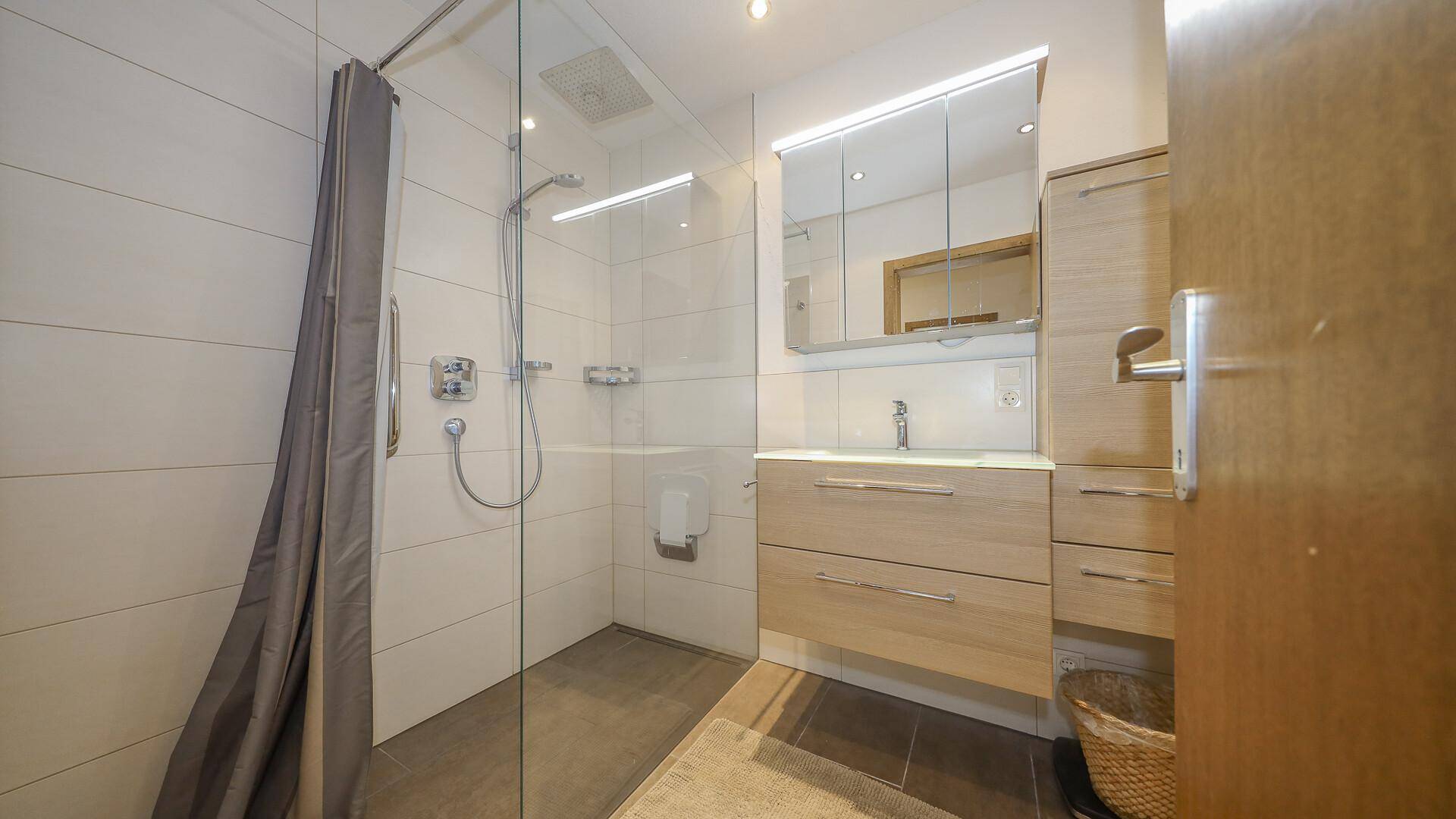 Modernes Badezimmer mit begehbarer Dusche, Waschtisch, Spiegelschrank und hellen Fliesen.
