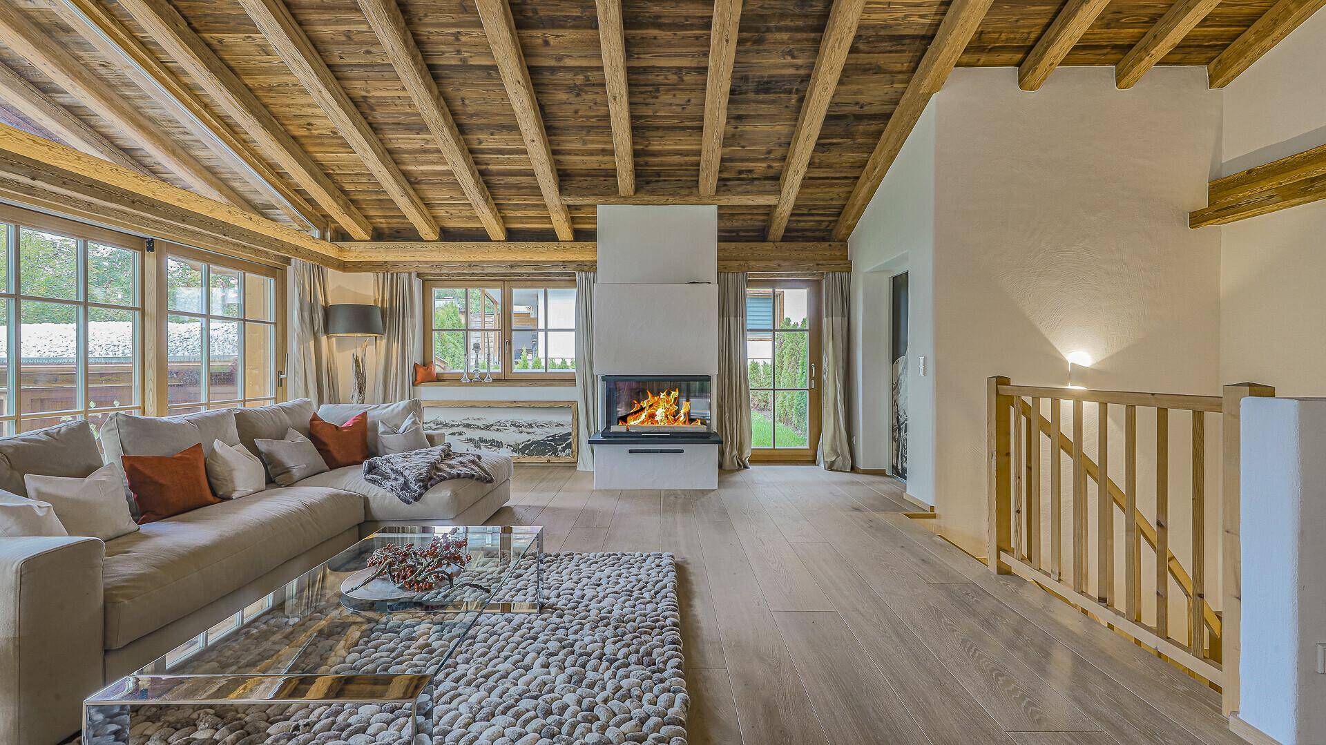 Geräumiges Wohnzimmer mit Kamin, Holzbalkendecke und Zugang zu weiteren Bereichen des Hauses.