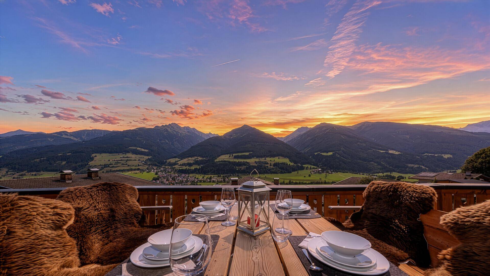 Terrasse bei Sonnenuntergang mit gedecktem Tisch und spektakulärem Blick auf die Alpen.
