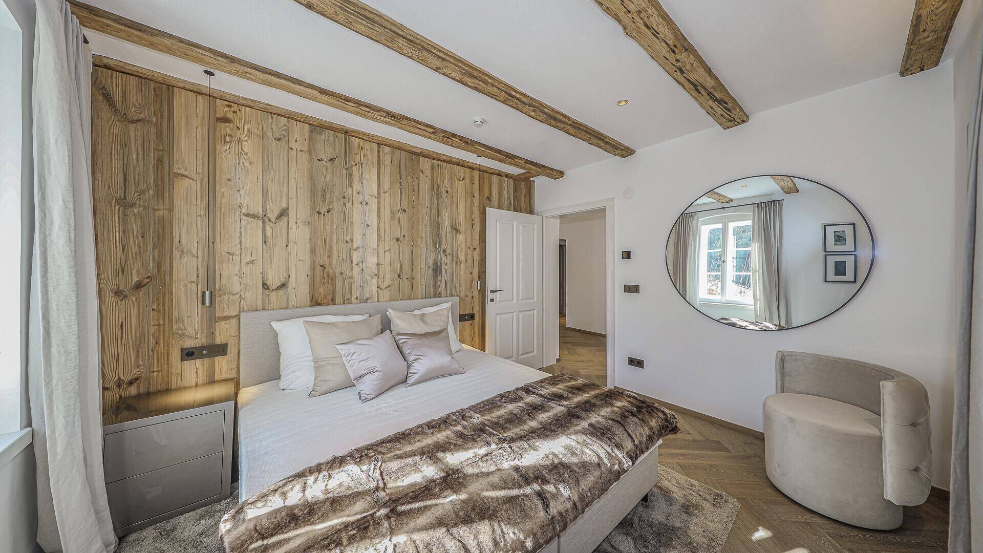 Stilvolles Schlafzimmer mit Holzwand, sichtbaren Balken und großem Spiegel.