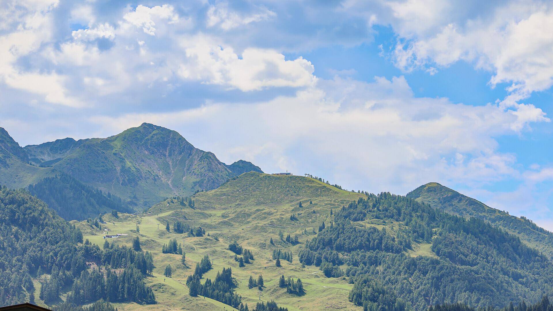 Sanfte grüne Berge mit Wäldern und Wiesen unter einem teilweise bewölkten Himmel.