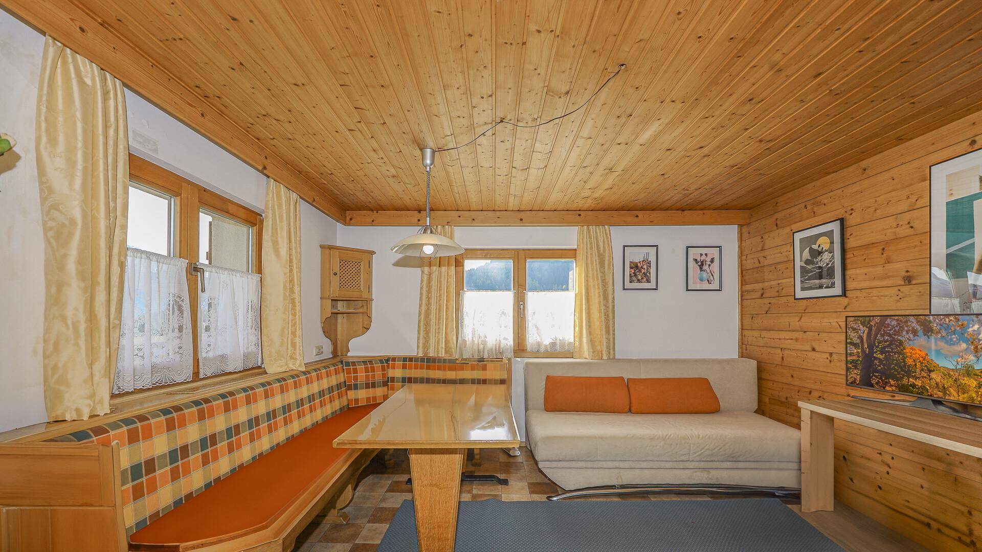 Traditioneller Wohn-Essbereich im alpinen Stil mit Holztäfelung, Sitzbank und karierten Polstern.