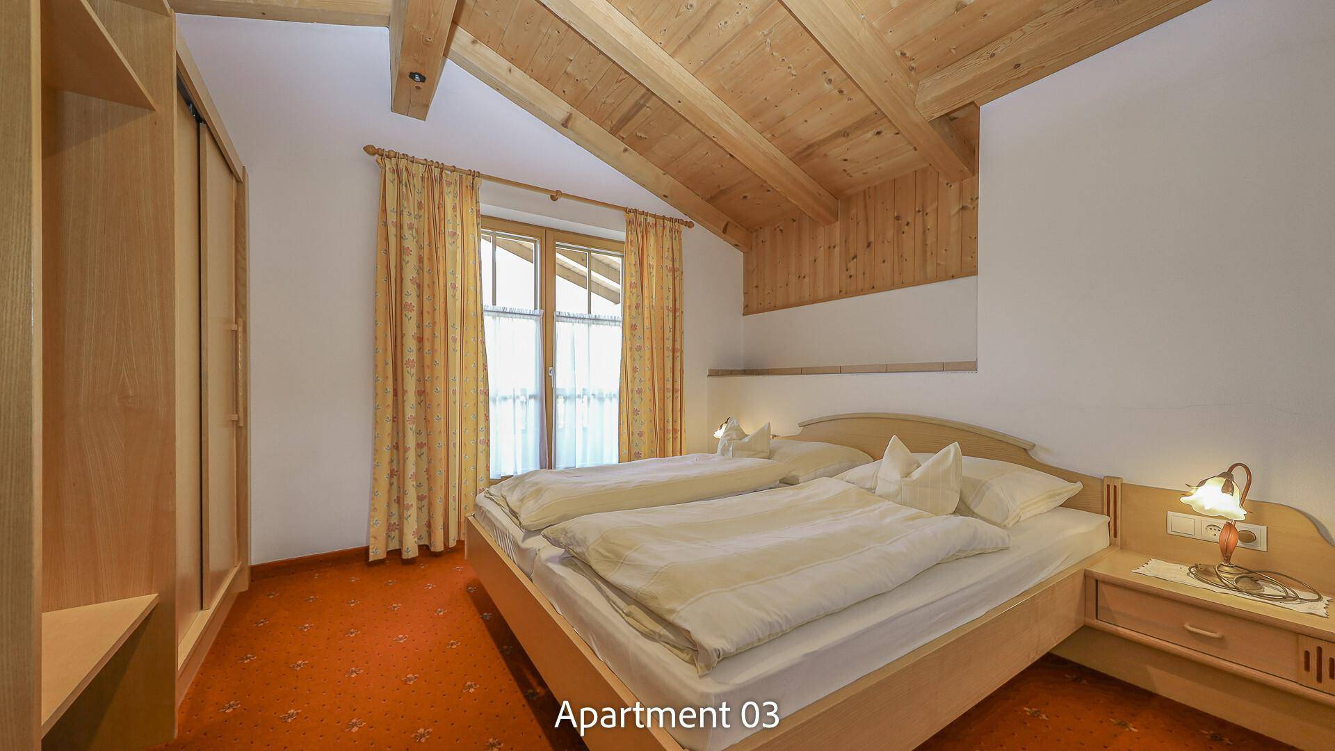 Geräumiges Schlafzimmer mit Doppelbett, Holzmöbeln und Teppichboden unter Dachschräge.