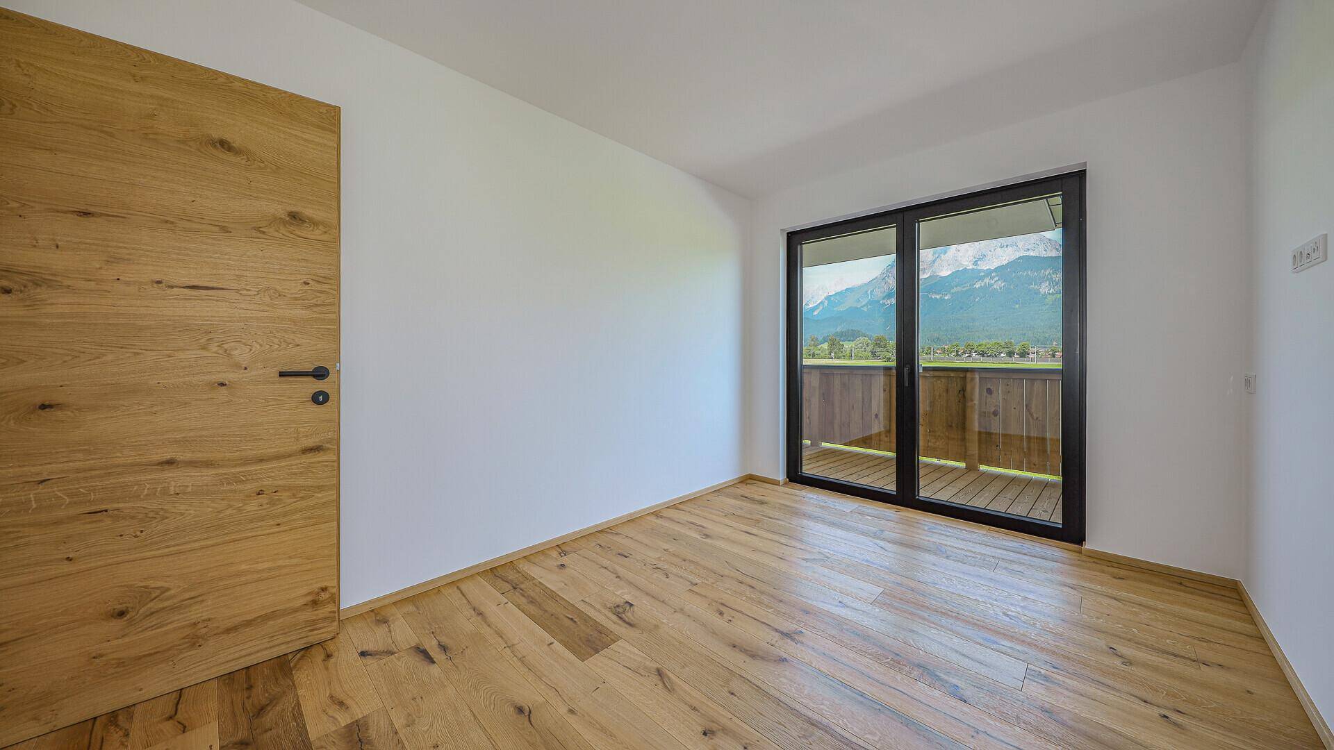 Unmöblierter Raum mit Holzboden und Holztür, bietet Zugang zu einem Balkon mit Bergblick.