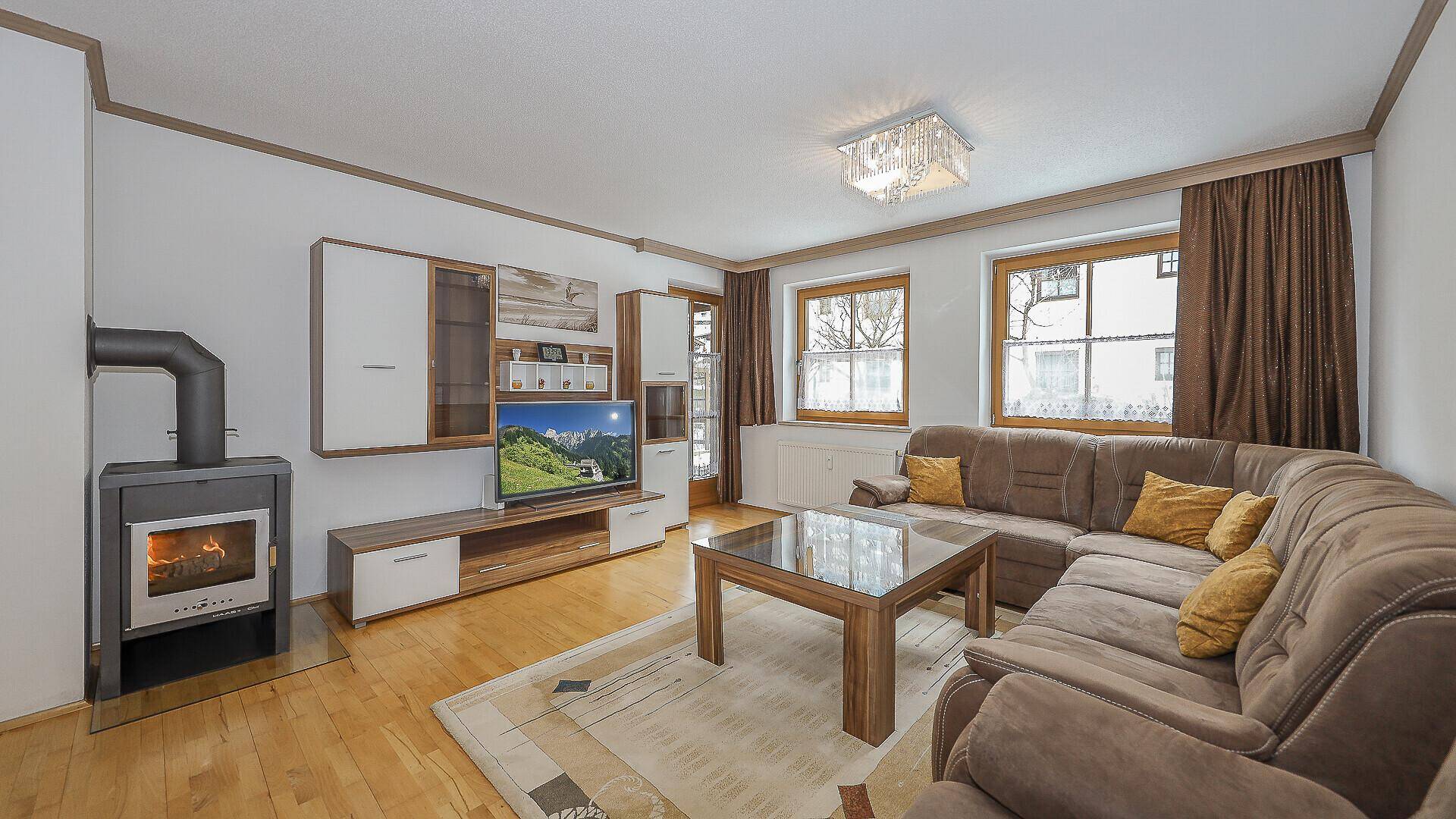 Gemütliches Wohnzimmer mit Kaminofen, Ecksofa und hellem Parkettboden.