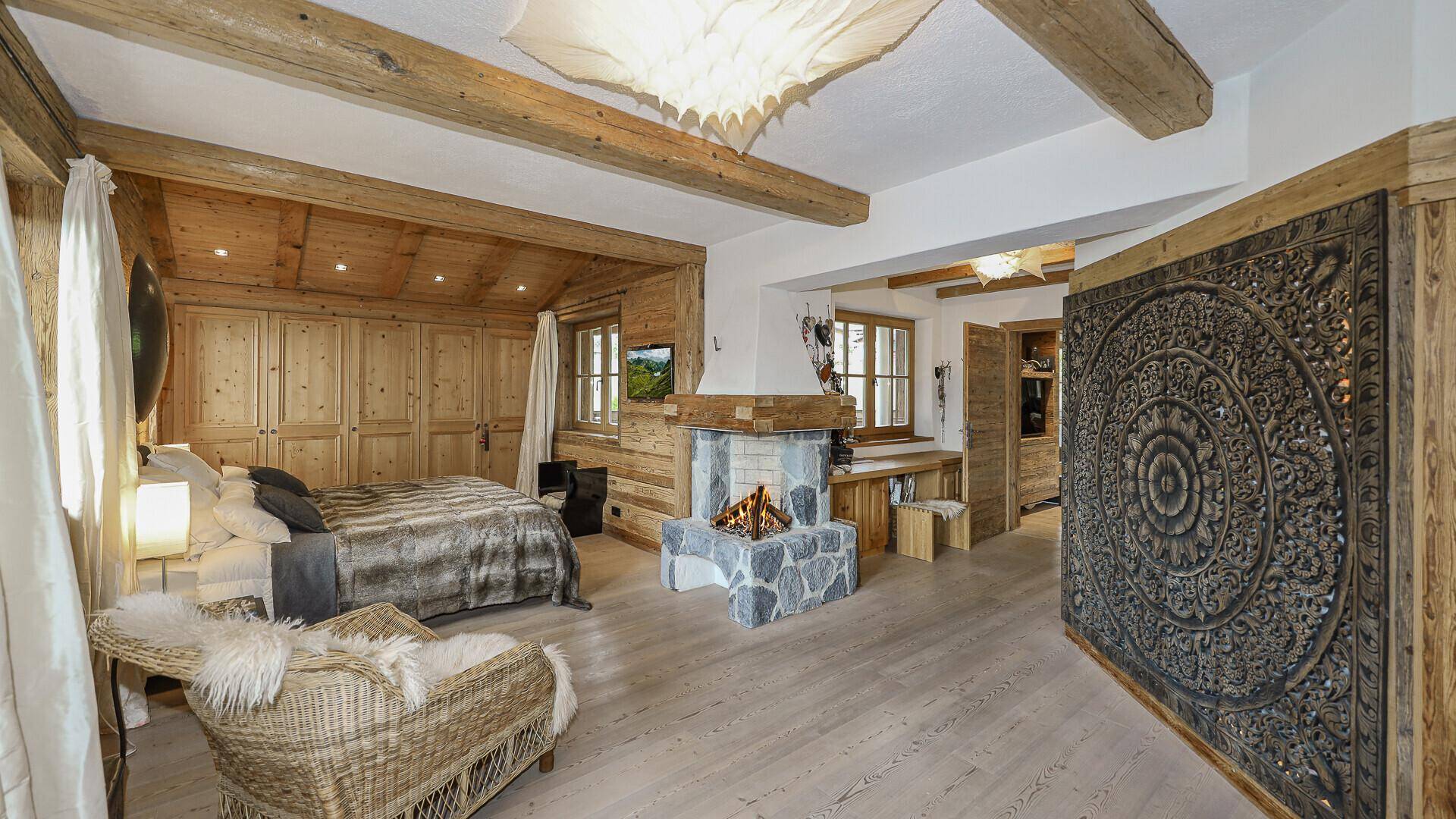 Großes Schlafzimmer im alpinen Stil mit Holzbalken, Kamin und integrierten Schränken.