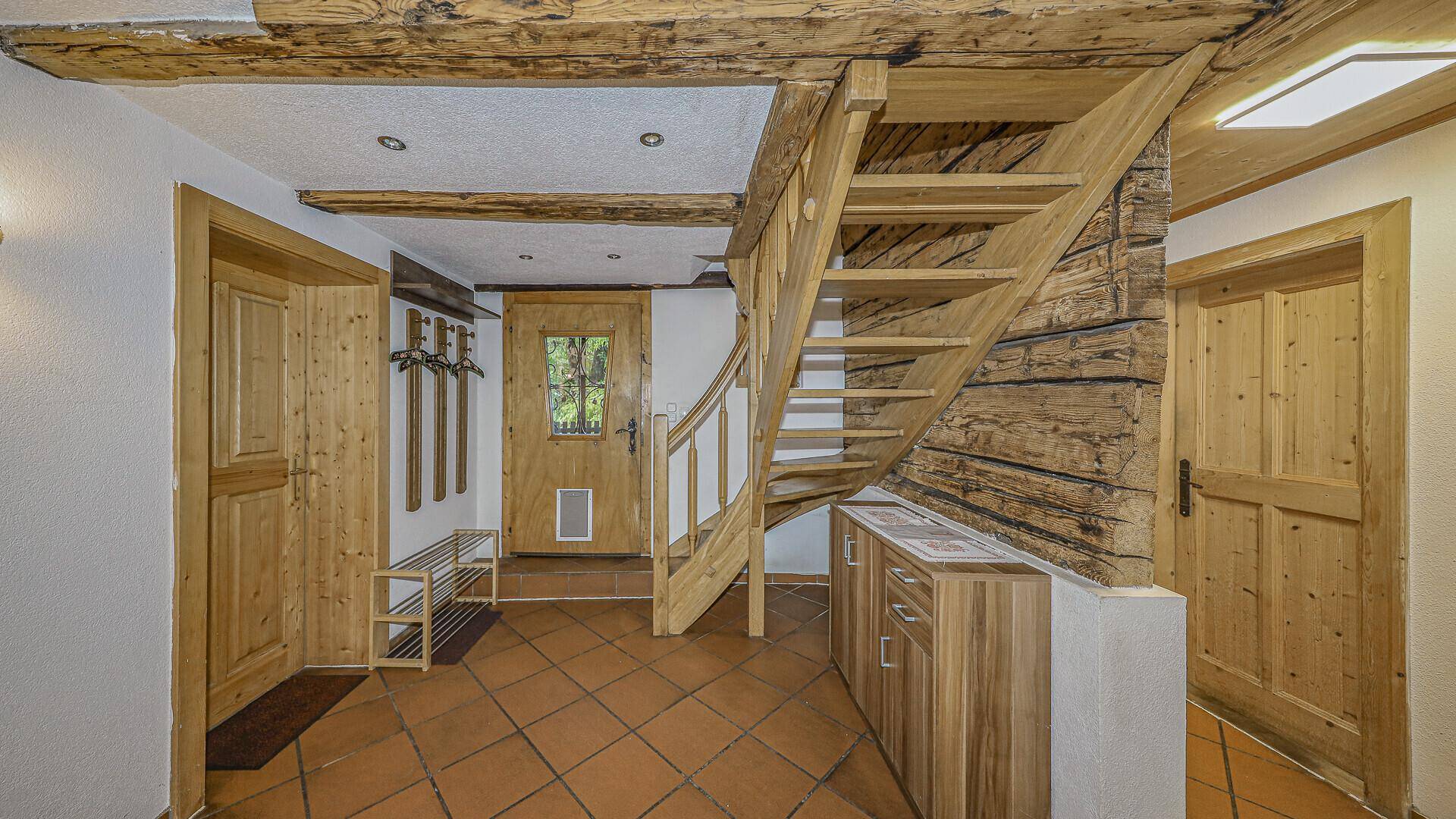 Eingangsbereich mit Holztreppe, gefliestem Boden und rustikalen Holzelementen.