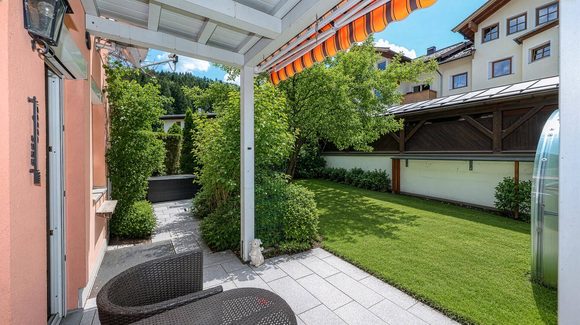Überdachte Terrasse mit Gartenmöbeln und direktem Zugang zum gepflegten Rasenbereich.