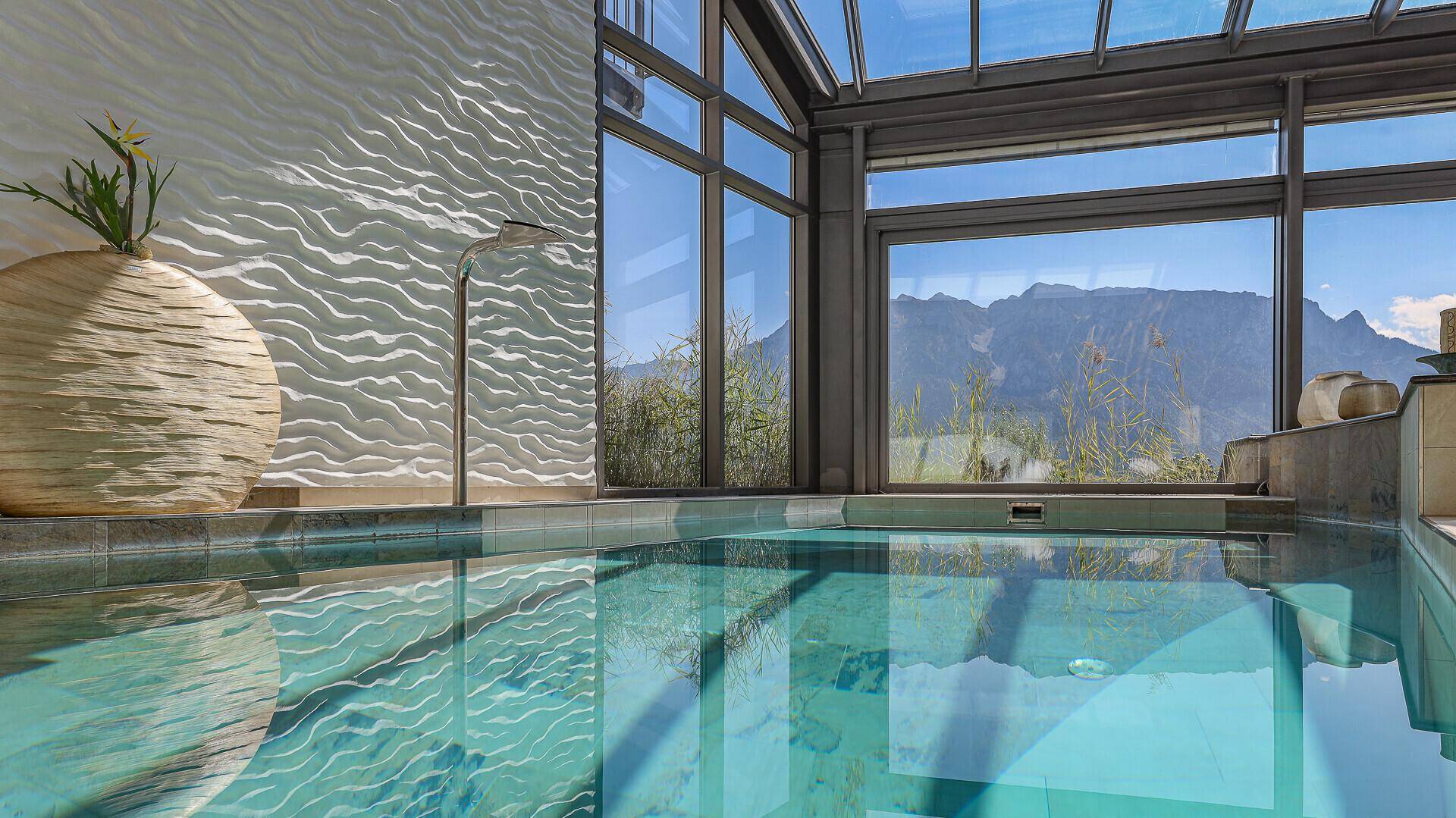 Detailansicht des Innenpools mit klarem Wasser, Wandgestaltung und Bergblick durch große Fenster.