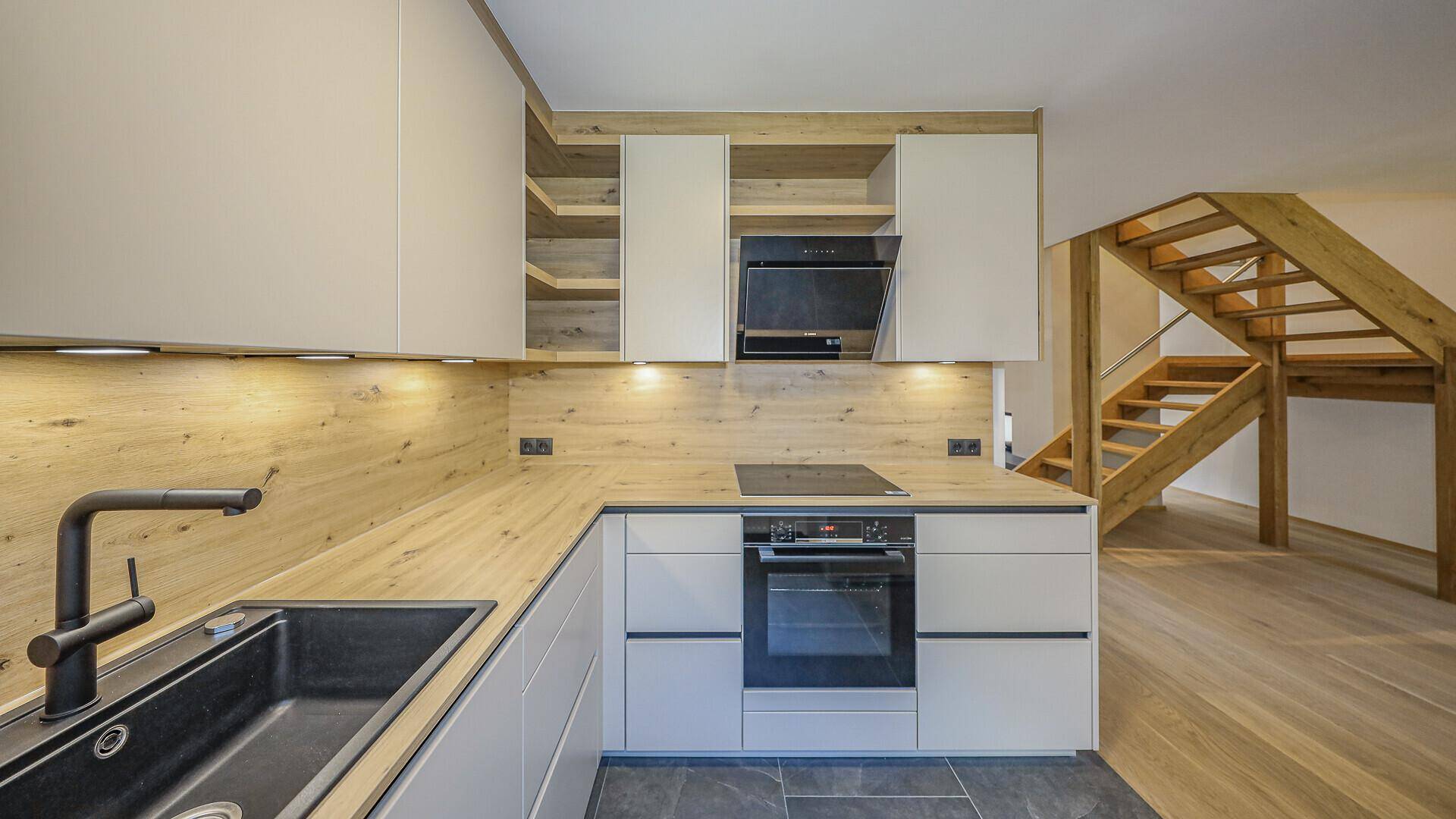 Helle Einbauküche mit Holzarbeitsplatten, modernen Geräten und Blick auf die Holztreppe.