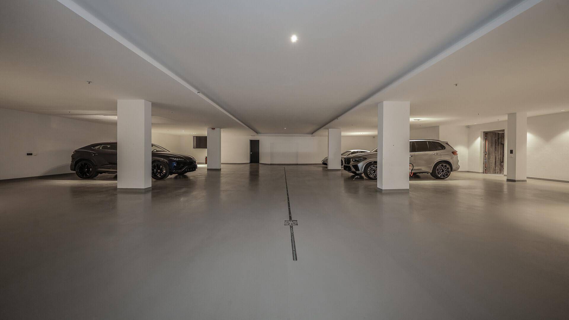 Geräumige Tiefgarage mit mehreren Luxusautos, weißen Säulen und glattem Betonboden.