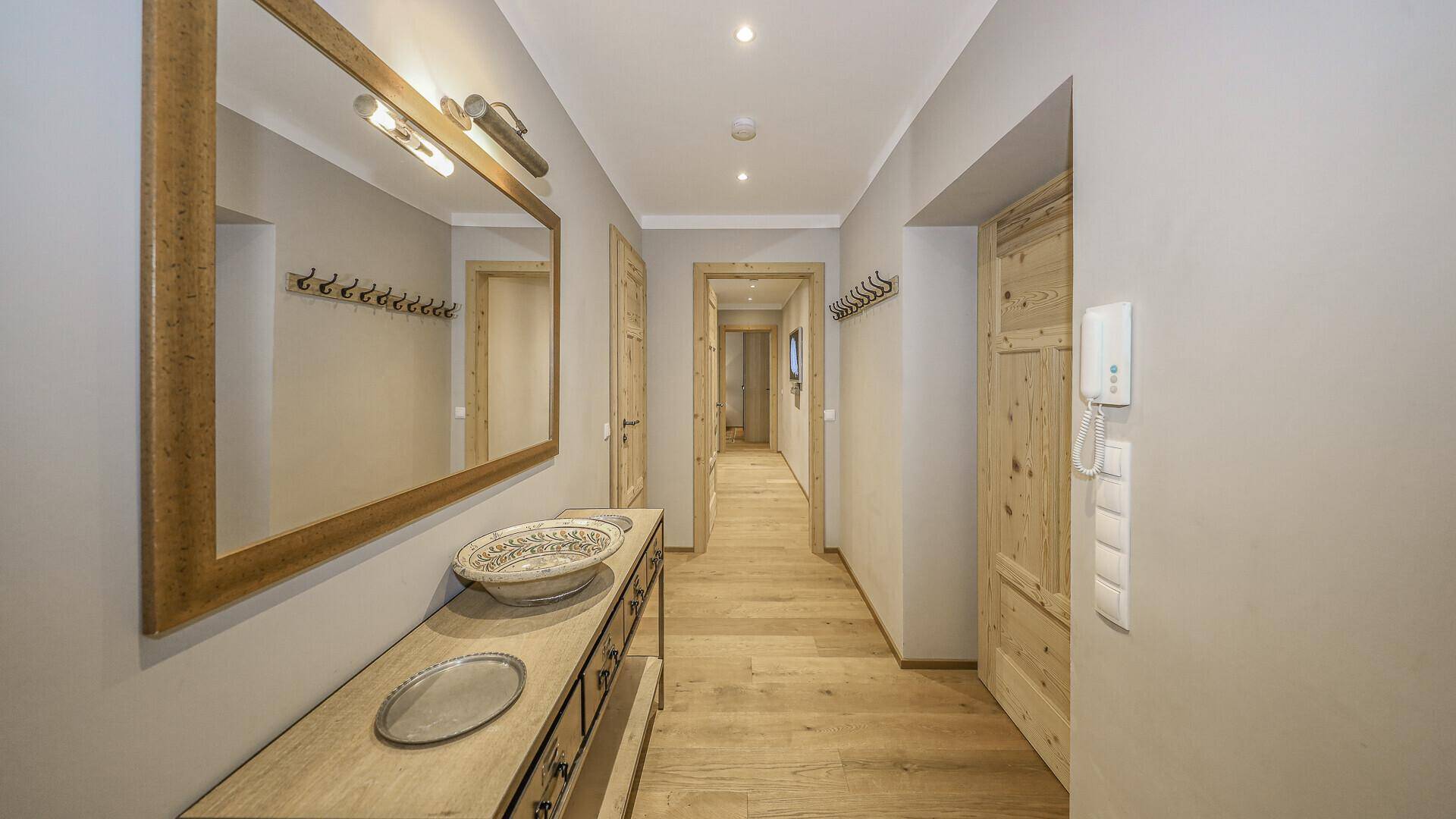 Heller Flur mit Holzmöbeln, Spiegel und Garderobe im traditionellen alpinen Stil.