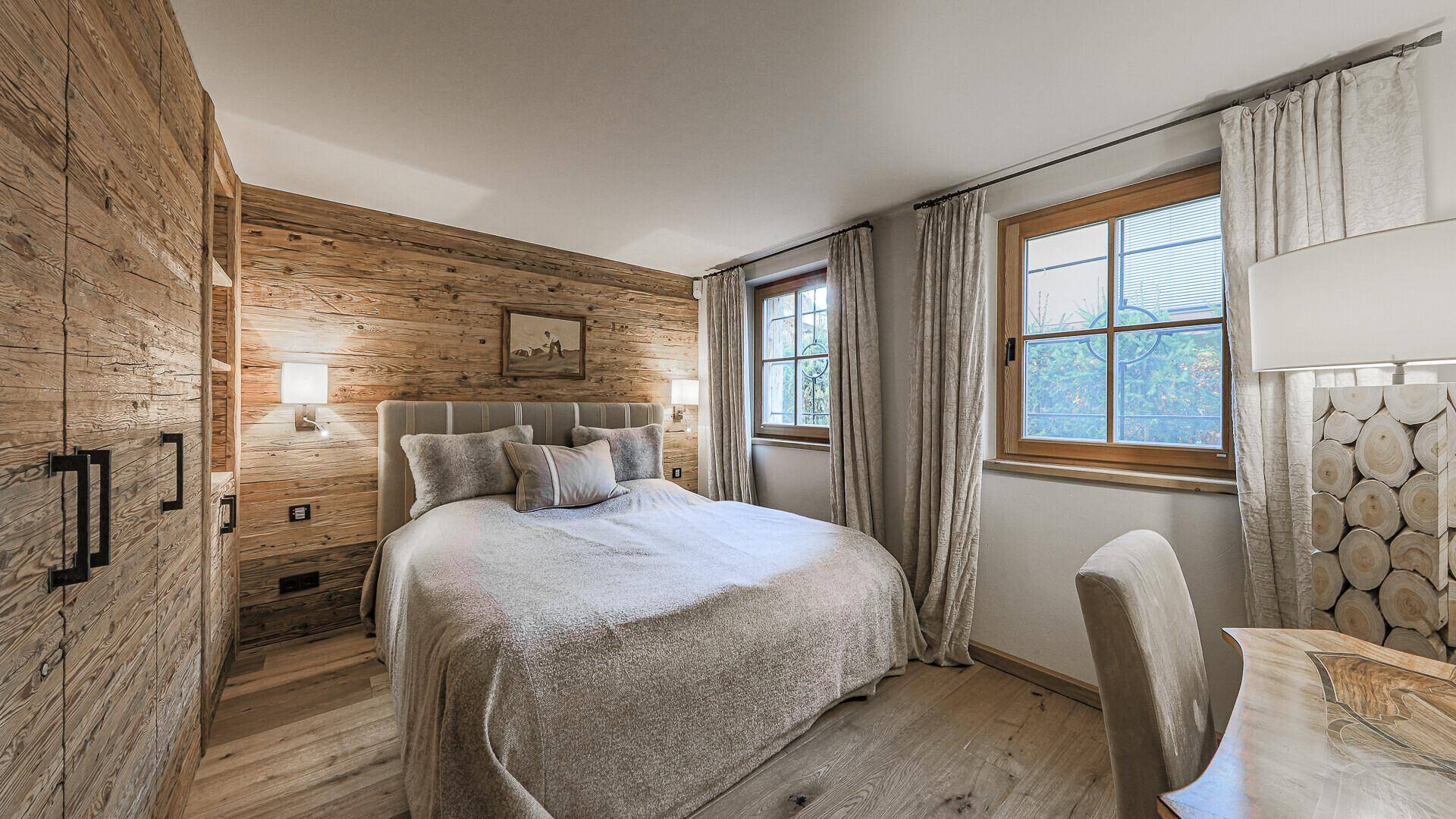 Schlafzimmer im Alpenstil mit Holzwand, Doppelbett und Blick in den Garten.