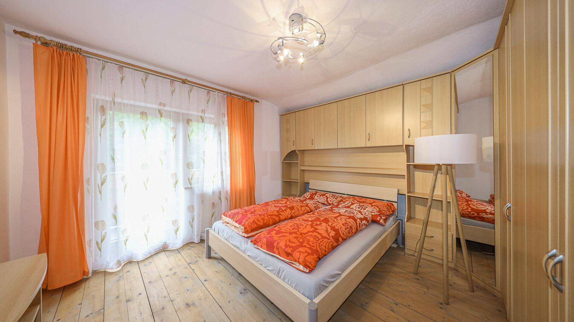 Gemütliches Schlafzimmer mit Holzdielenboden, Einbauschränken und farbenfrohen Vorhängen.