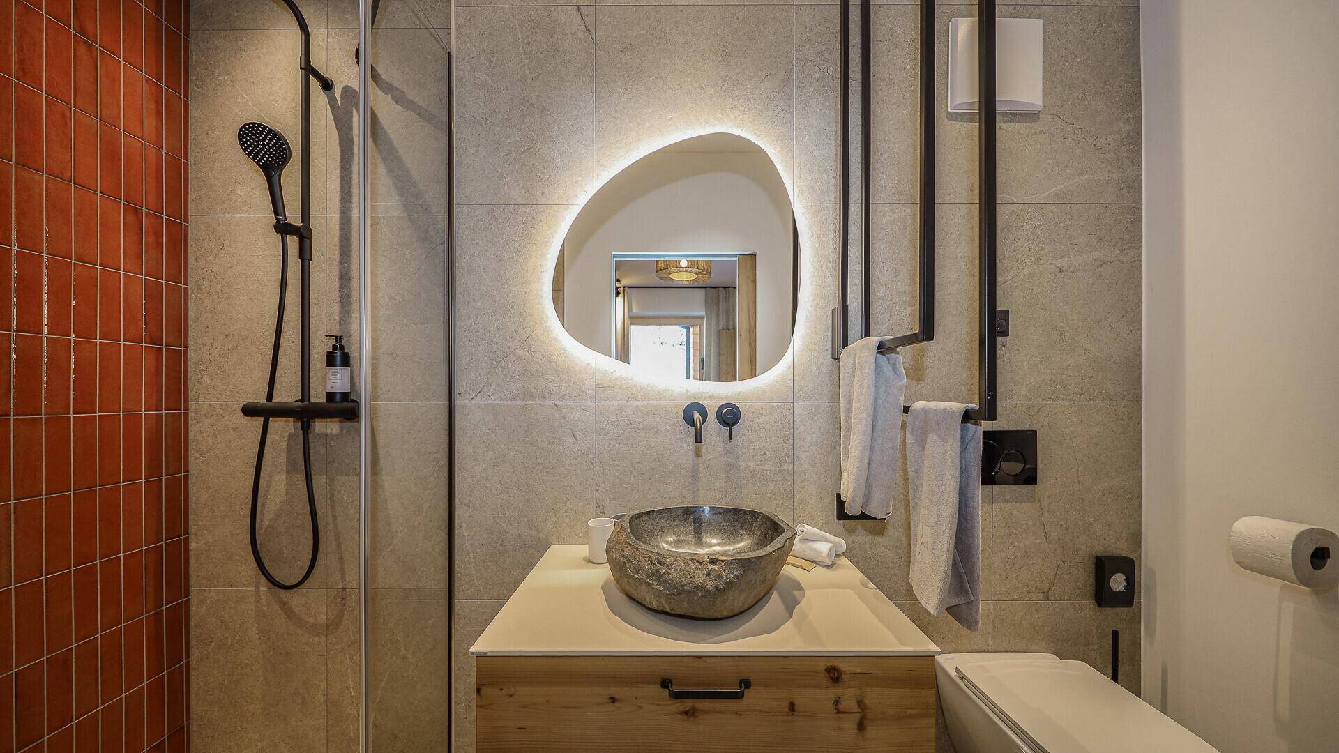 Modernes Badezimmer mit grauen und orangefarbenen Fliesen, Natursteinwaschbecken und Dusche.
