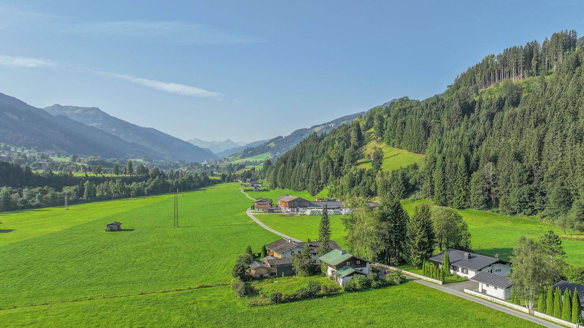 Luftaufnahme des Anwesens in einer idyllischen Bergregion mit weiten grünen Wiesen und bewaldeten Hängen.