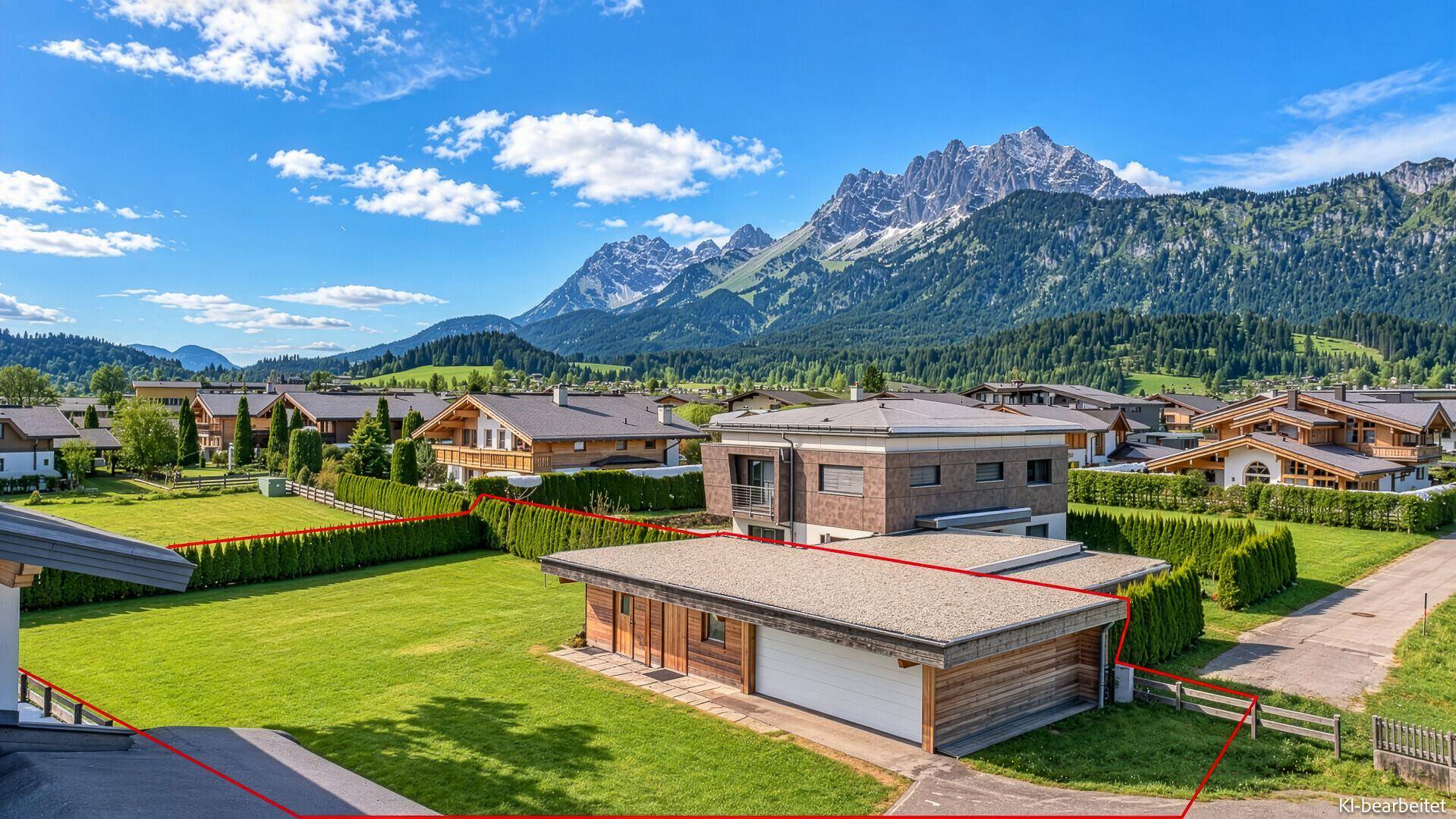 Luftaufnahme eines Anwesens mit modernem Haus und Nebengebäude, umgeben von Grünflächen und Bergen.