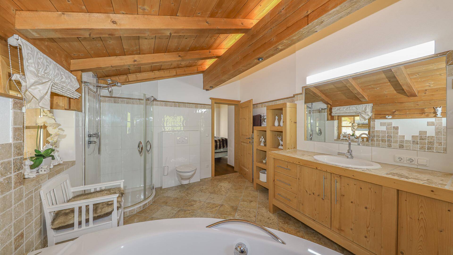 Helles Badezimmer mit Doppelwaschbecken, Dusche, Fliesenboden und Holzbalkendecke.