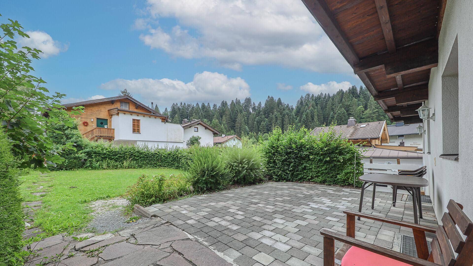 Gepflasterte Terrasse mit Gartenmöbeln und Zugang zum grünen Gartenbereich.
