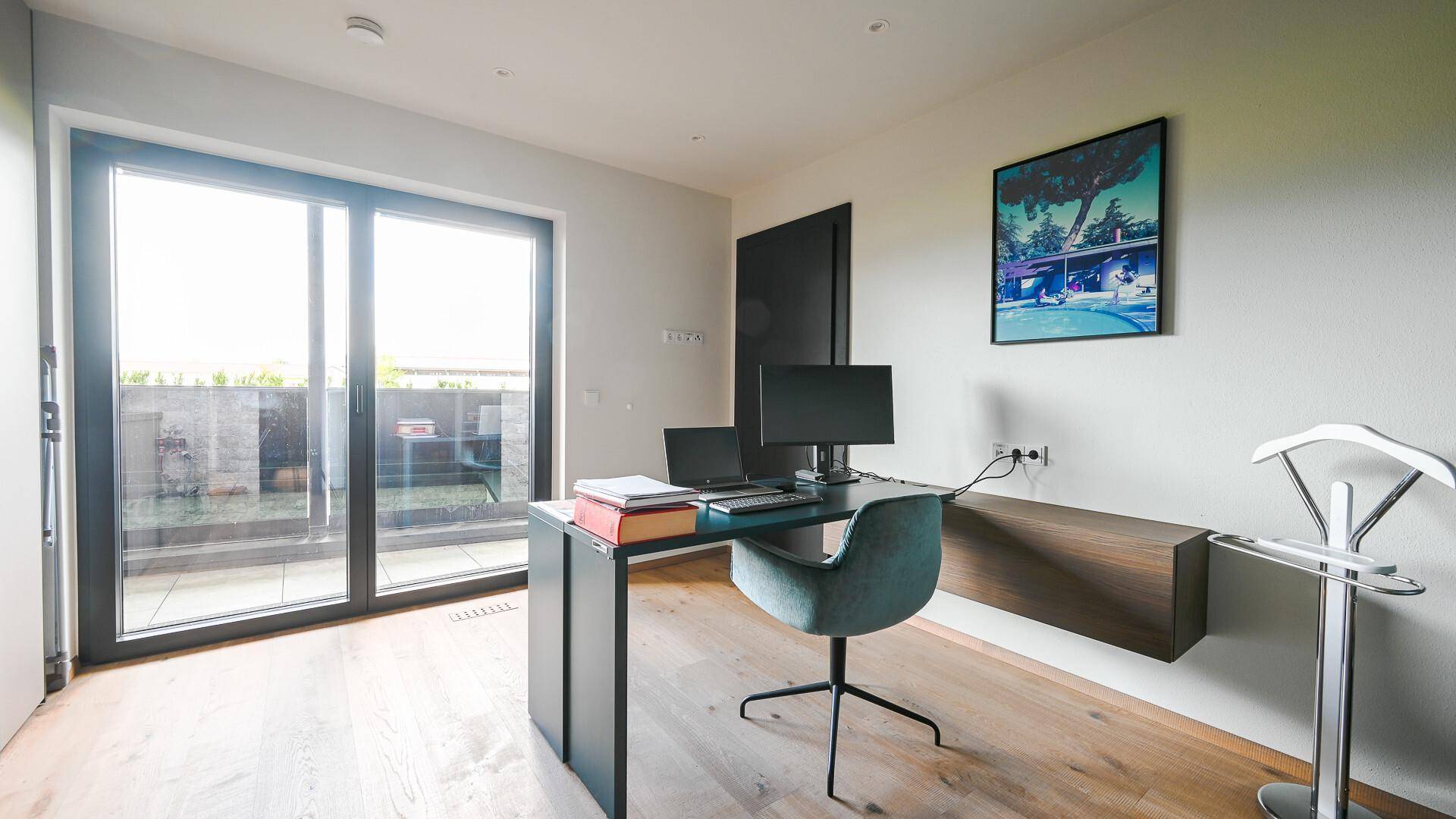 Helles Arbeitszimmer mit Schreibtisch, Holzboden und Zugang zu einer Außenterrasse.