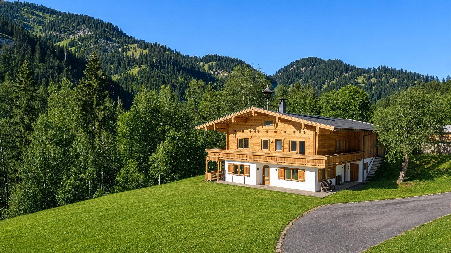 Charmantes Holzchalet in idyllischer Berglandschaft mit grünen Wäldern und Wiesen unter blauem Himmel.