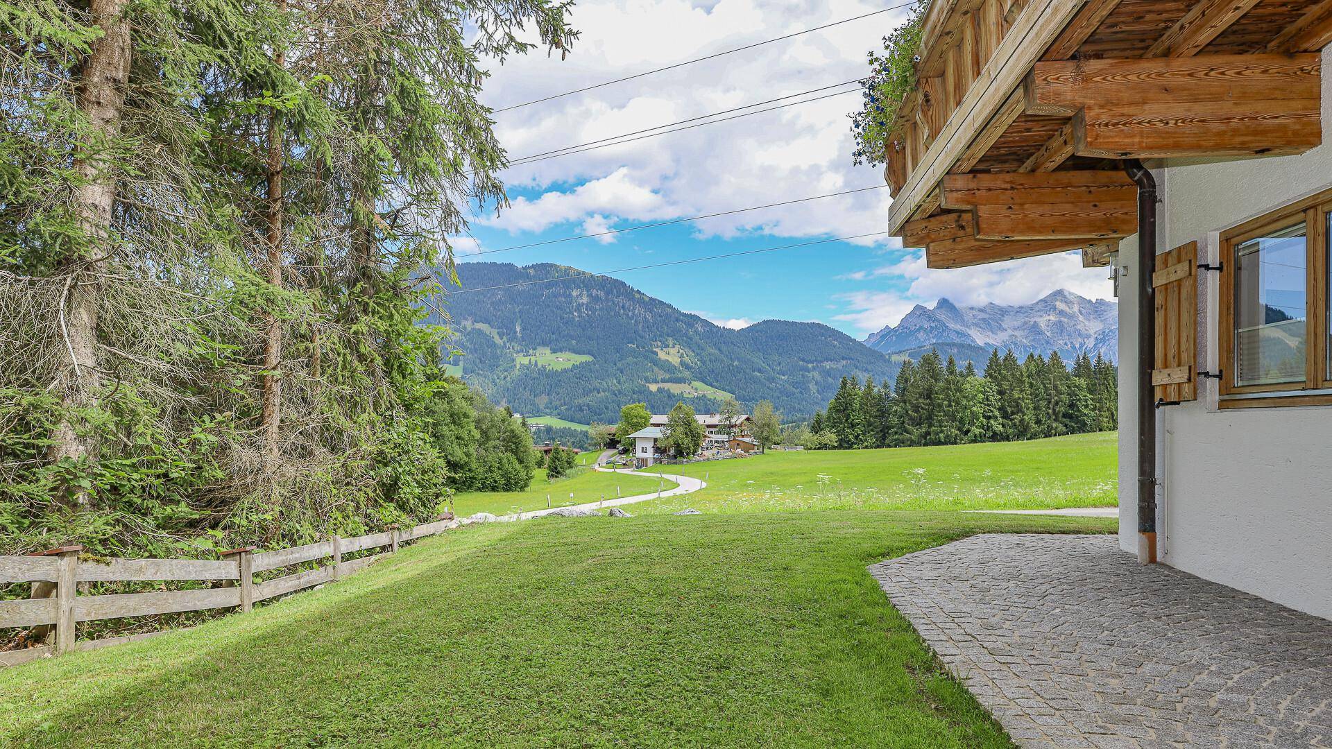 Gepflegter Rasenbereich neben dem Haus mit Blick auf die grüne Landschaft und Berge.