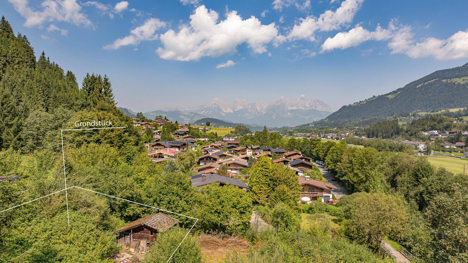 Panoramablick auf ein malerisches Dorf in den Bergen mit einem markierten Grundstück im Vordergrund.