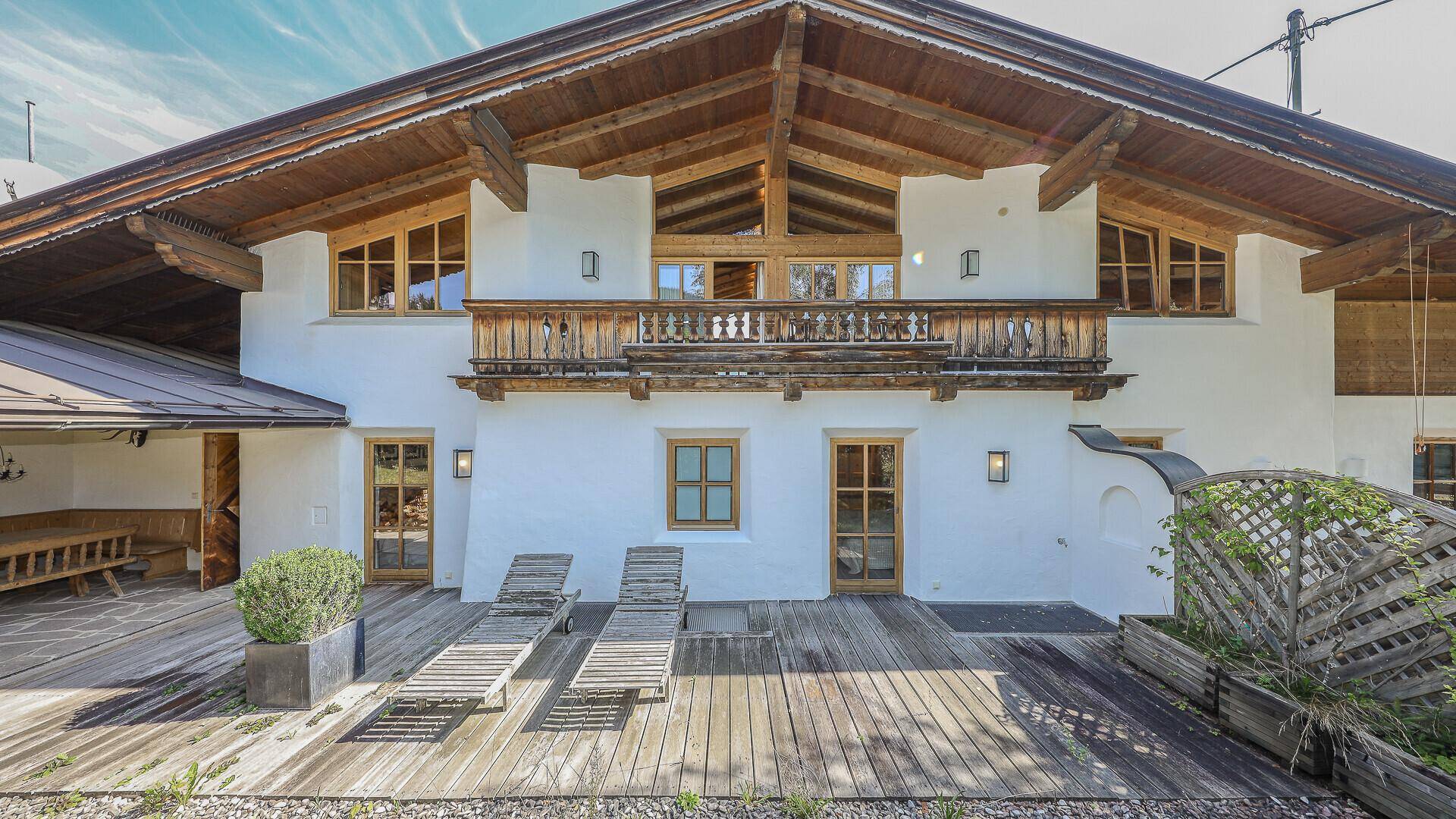 Große Holzterrasse mit Liegestühlen und Blick auf die Hausfassade und den Balkon.
