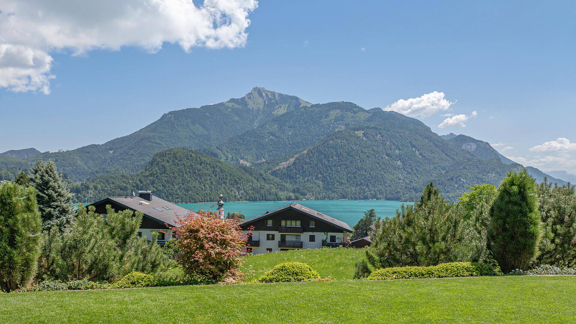 Weitläufiger Blick auf die grüne Landschaft, den See und die umliegenden Berge.