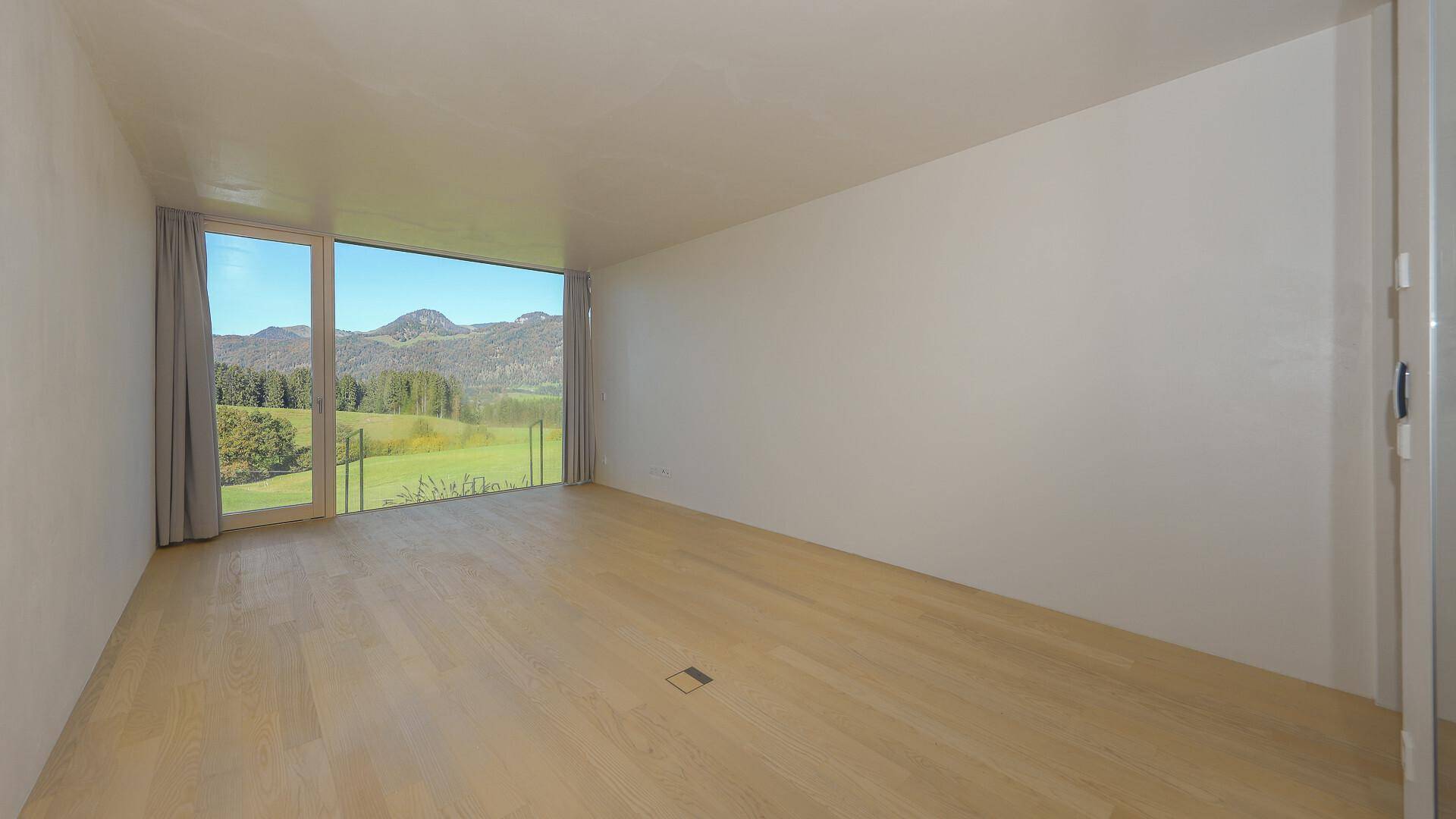 Helles, unmöbliertes Schlafzimmer mit Holzboden und raumhohen Fenstern mit Bergblick.