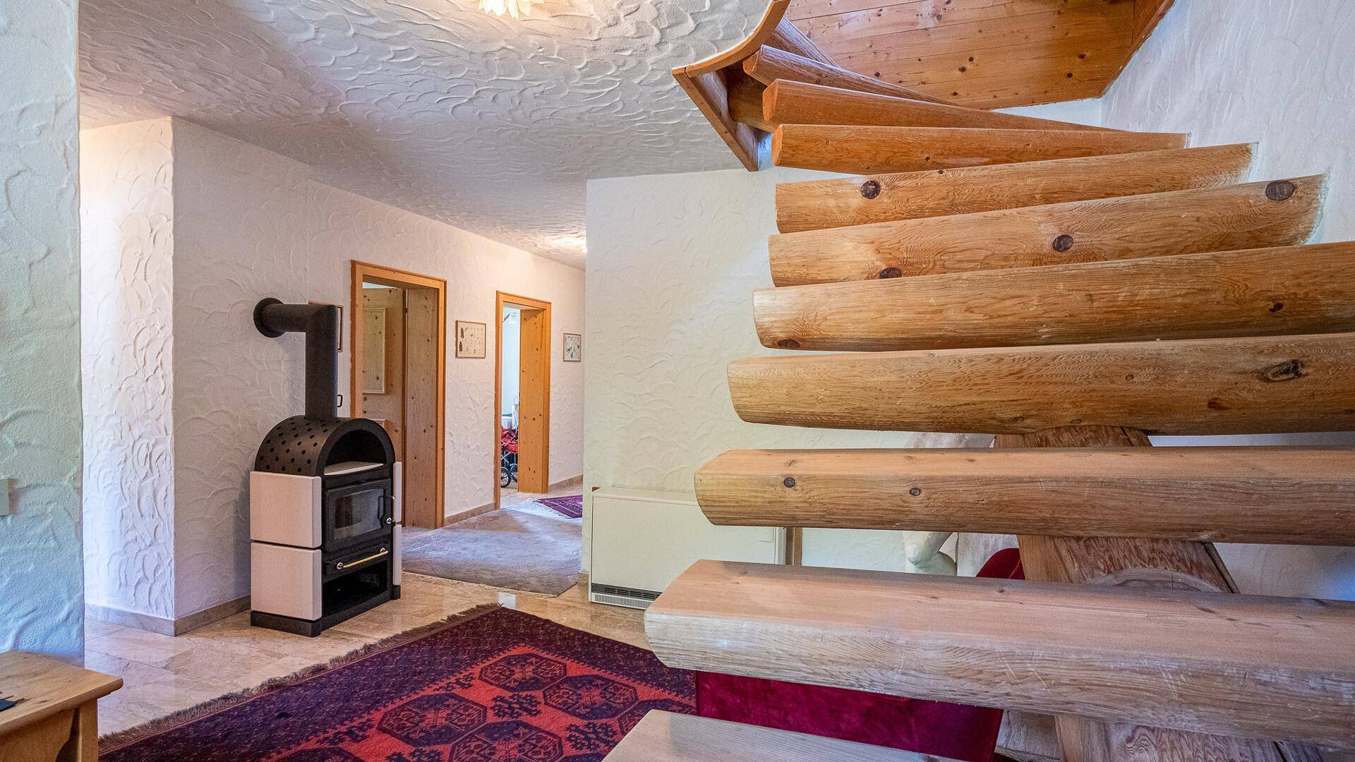 Eingangsbereich mit modernem Holzofen, rustikaler Holztreppe und gemustertem Teppichboden.
