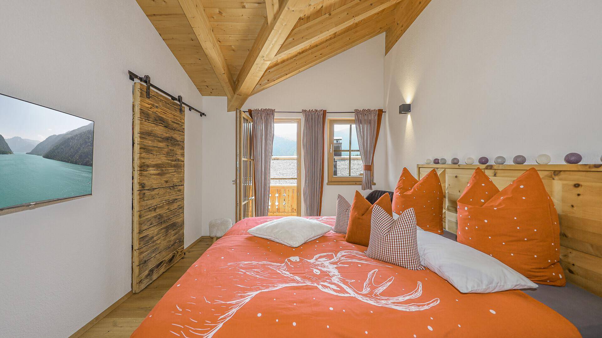 Helles Schlafzimmer mit hoher Holzdecke, Balkonzugang und Blick in die Natur.
