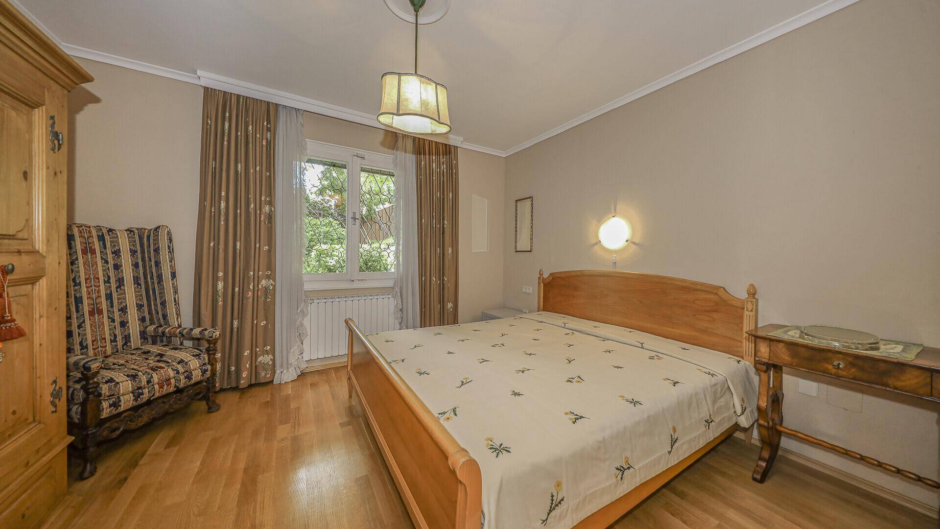 Helles Schlafzimmer mit Holzbett, Parkettboden und Fenster zum grünen Garten.