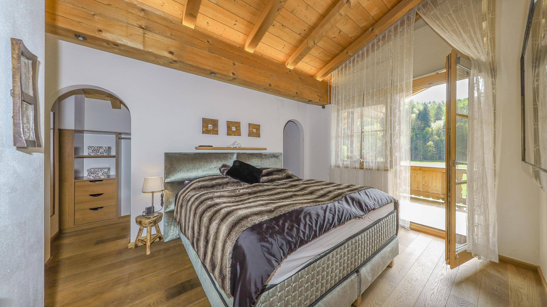 Schlafzimmer mit sichtbaren Holzbalken, Holzboden und Zugang zum Balkon mit Bergblick.