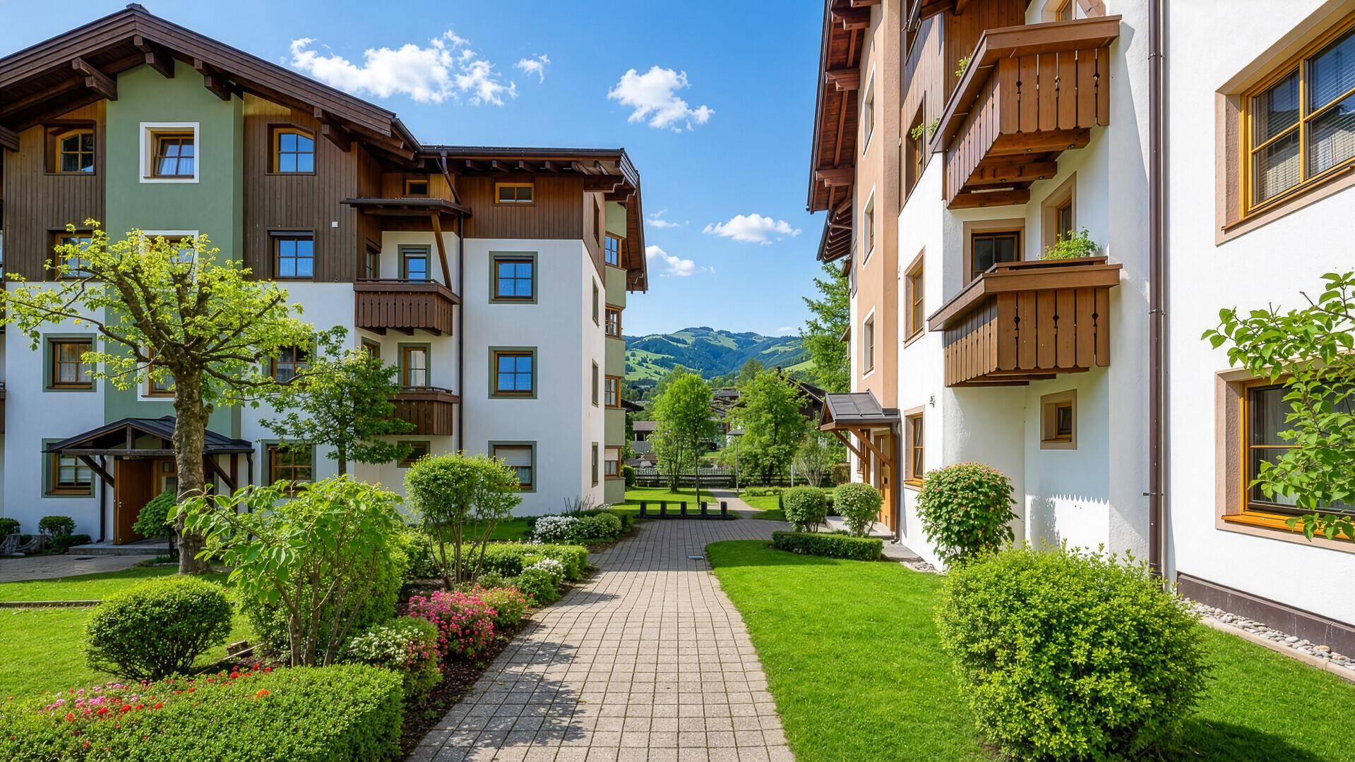 Wohnanlage mit gepflegten Grünflächen, Gehwegen und Bergblick im Hintergrund.