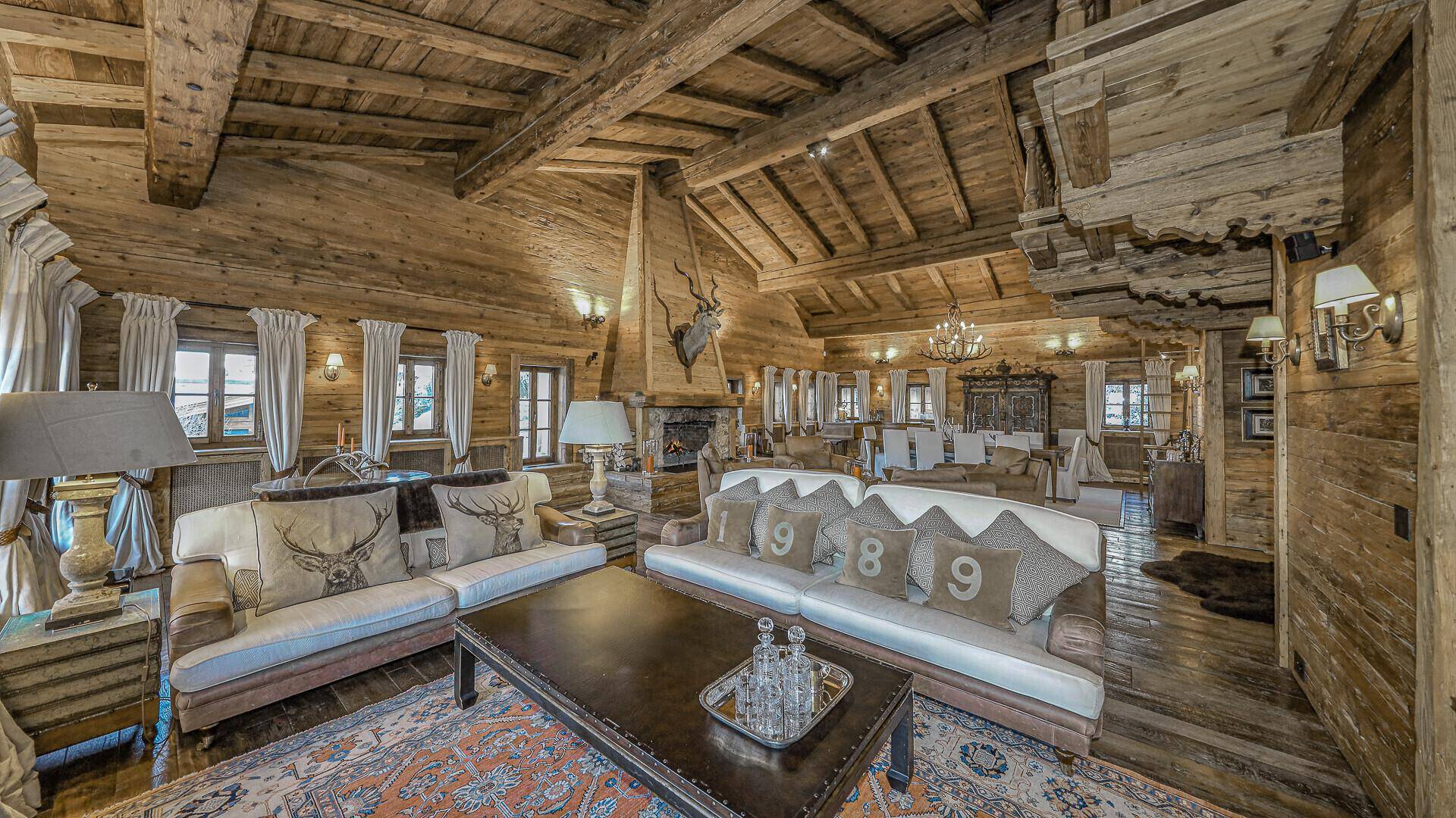 Großzügiger alpiner Wohn- und Essbereich mit Holzbalken, Kamin und gemütlichen Sofas.